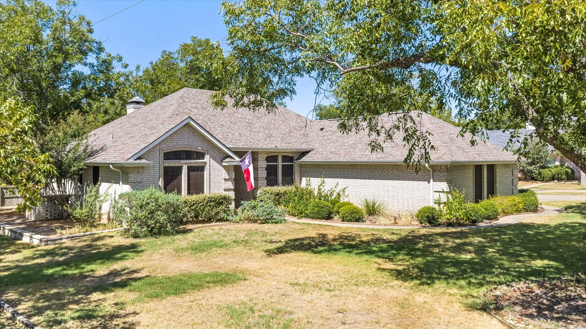 Light brick exterior, pitched shingle roof, mature landscaping, and an arched window detail
