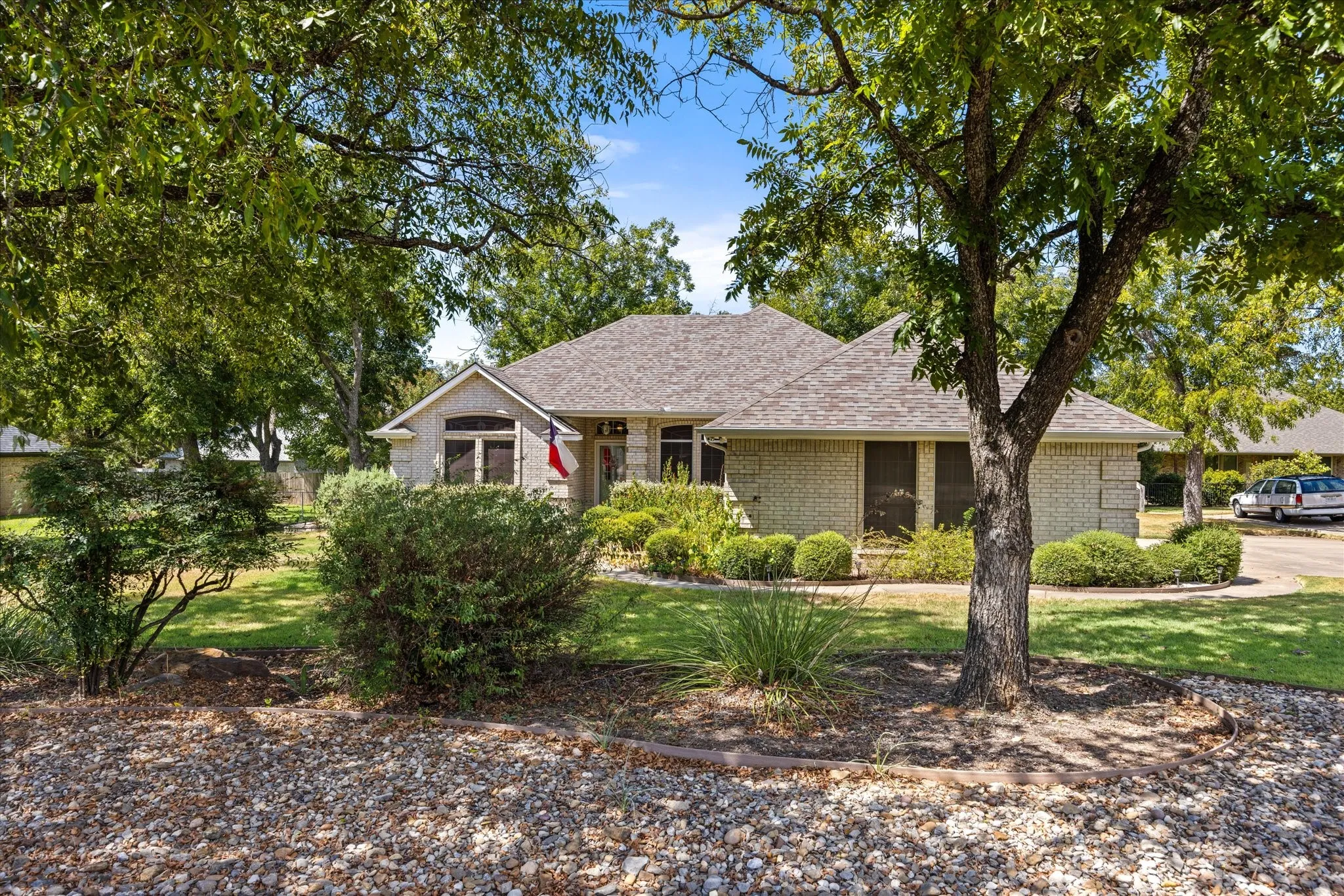 Brick exterior with a gabled roofline, mature trees, manicured lawn, and landscaped shrubbery