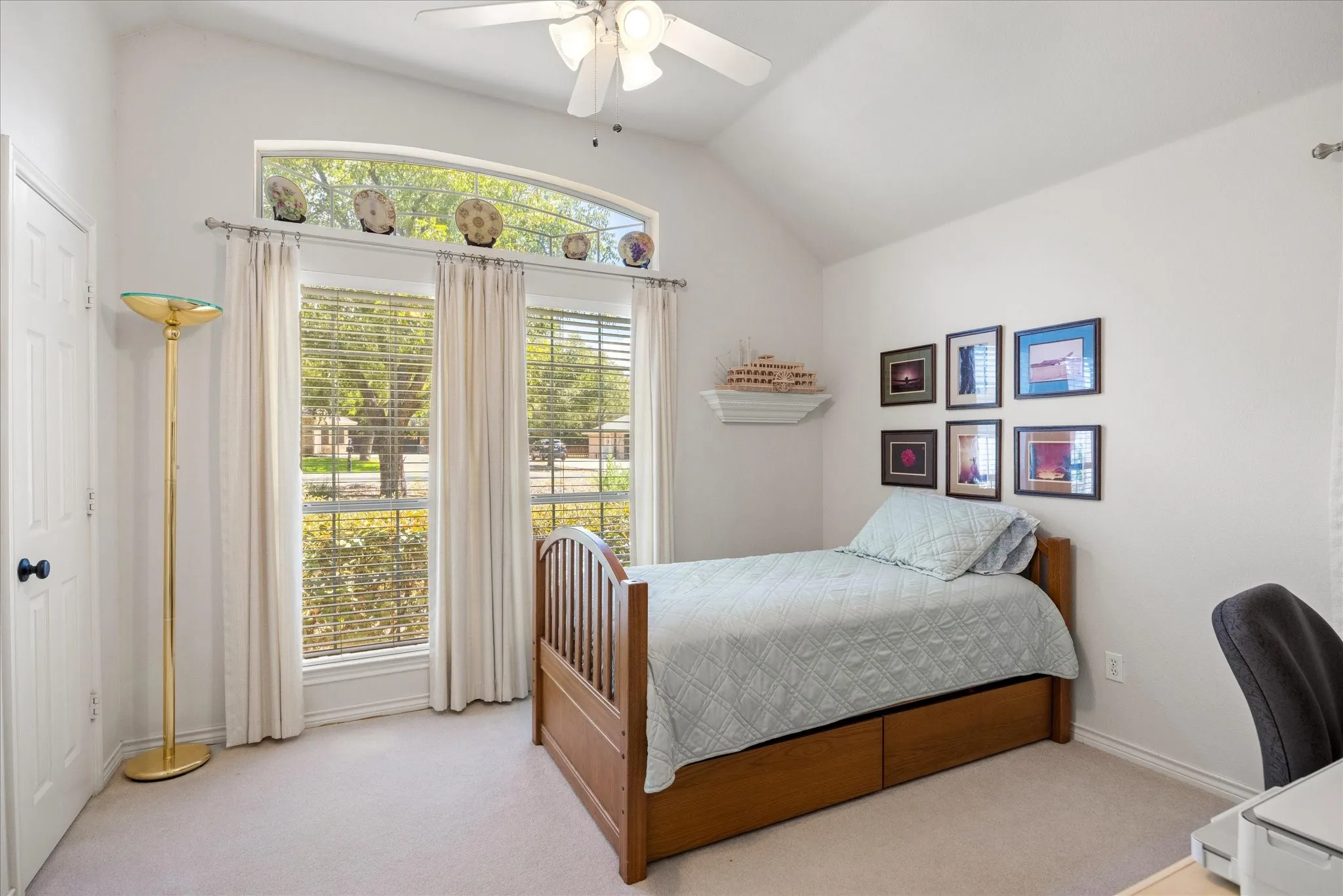 Vaulted ceiling with a ceiling fan, arched window, three vertical windows with blinds, built-in wall shelf, and light-toned carpet