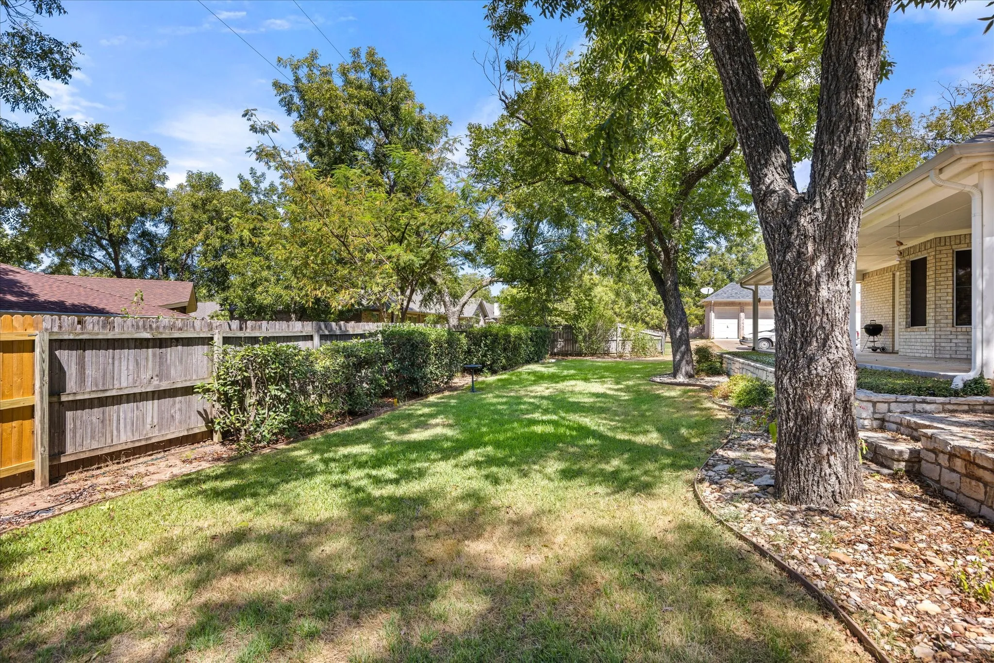 Expansive lawn featuring mature trees, a wood privacy fence, and manicured shrubs