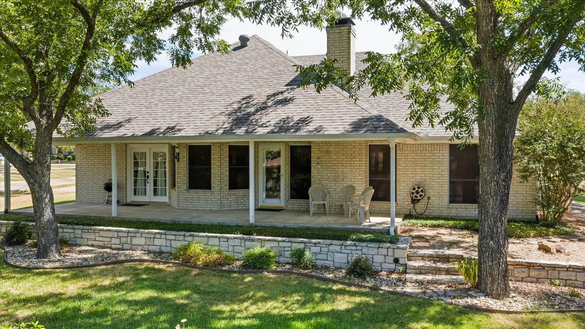 Covered patio with French doors, brick exterior, and stone retaining walls