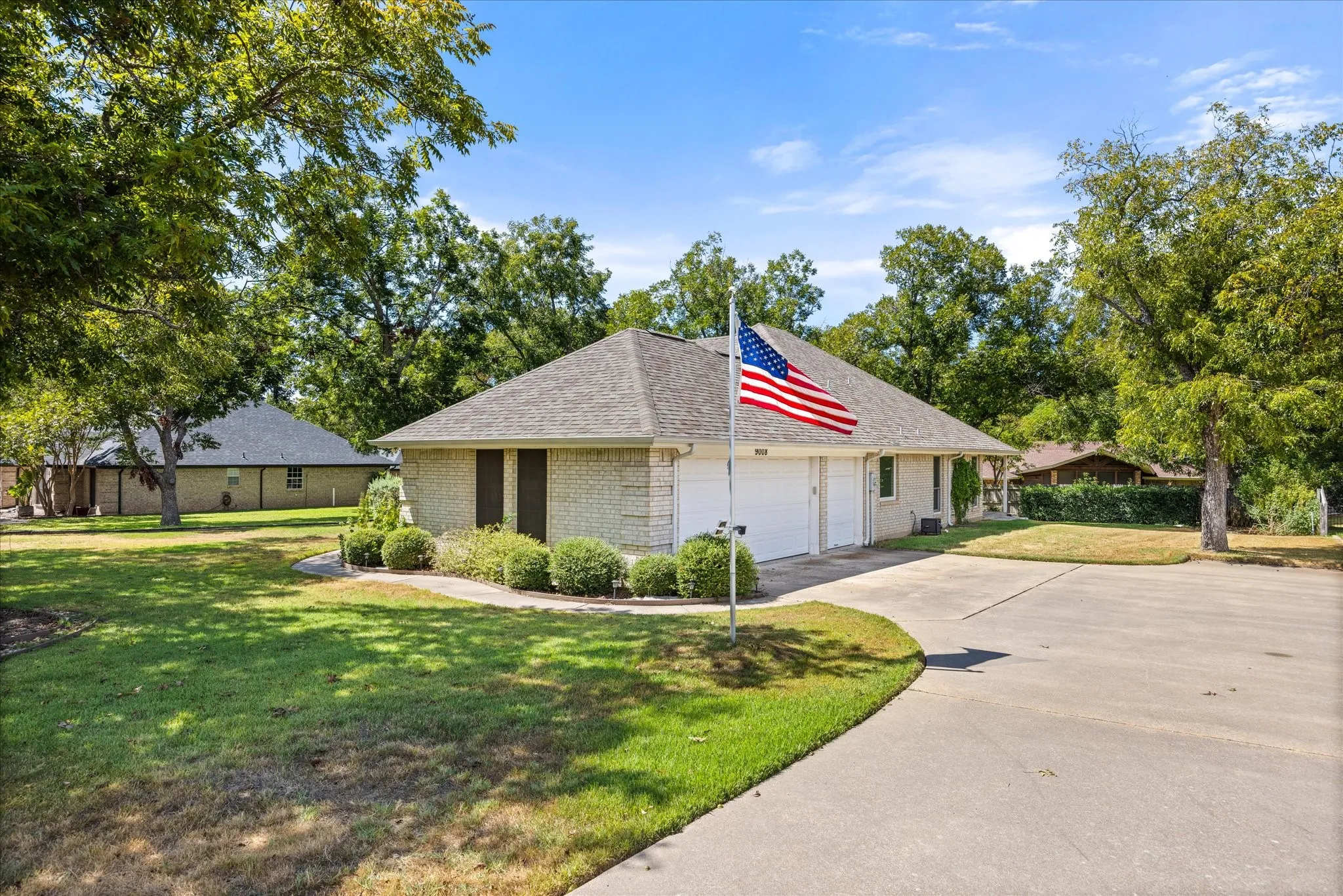 Brick exterior residence featuring a hip roof, attached garage with two doors, paved driveway, and established landscaping