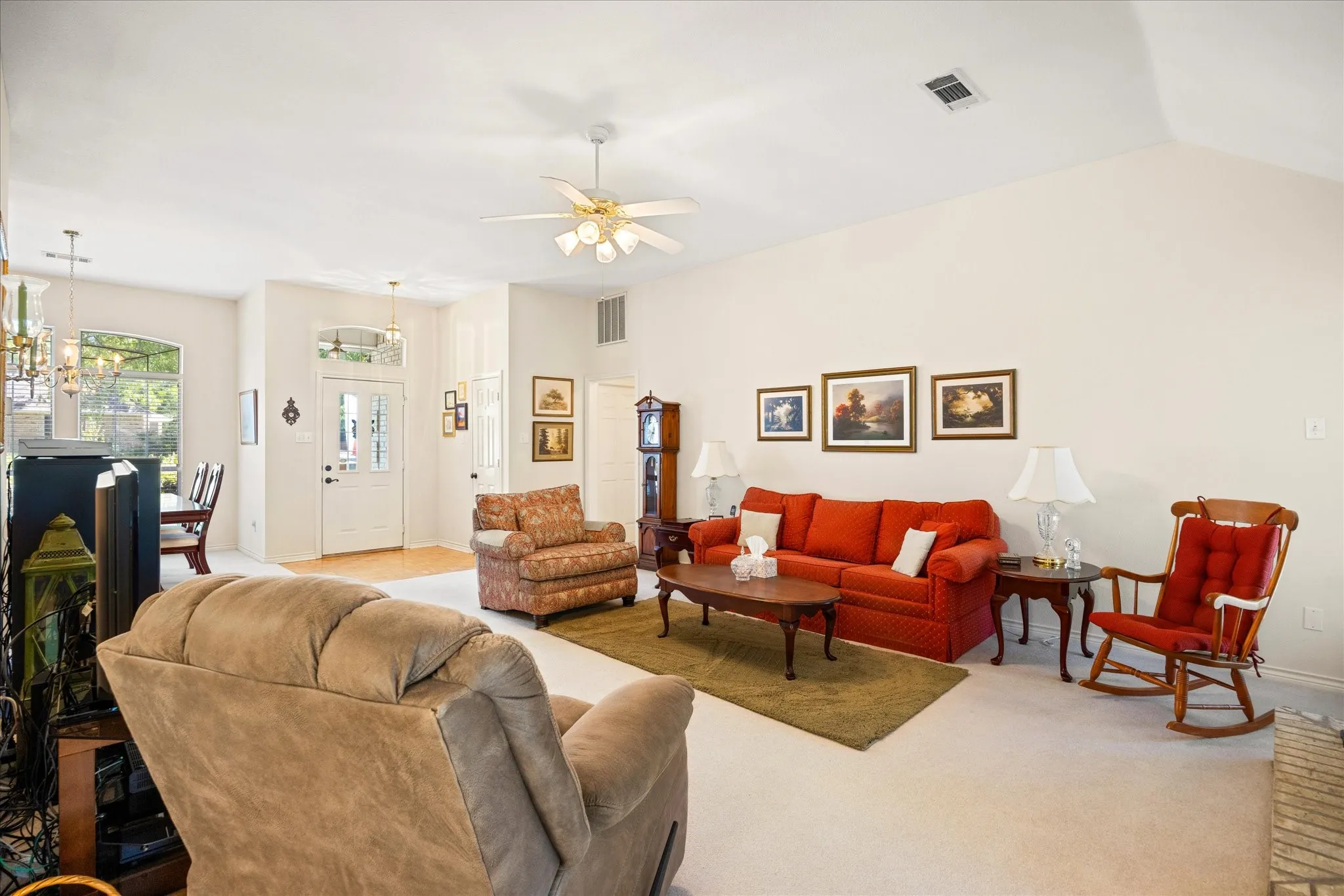 Vaulted ceiling with a ceiling fan, light-colored carpet flooring, entryway door with decorative glass inserts, and an arched window