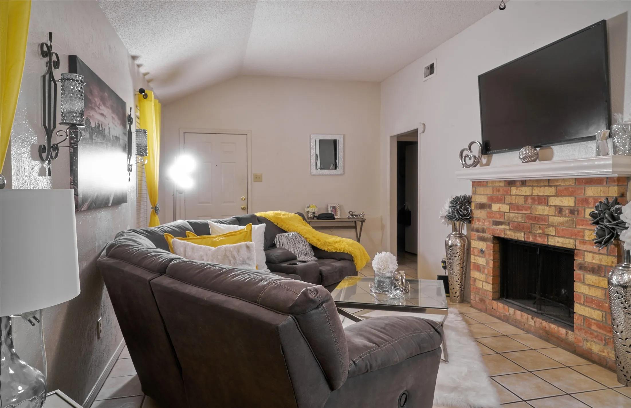 Living room with a brick fireplace, lofted ceiling, a textured ceiling, and light tile floors