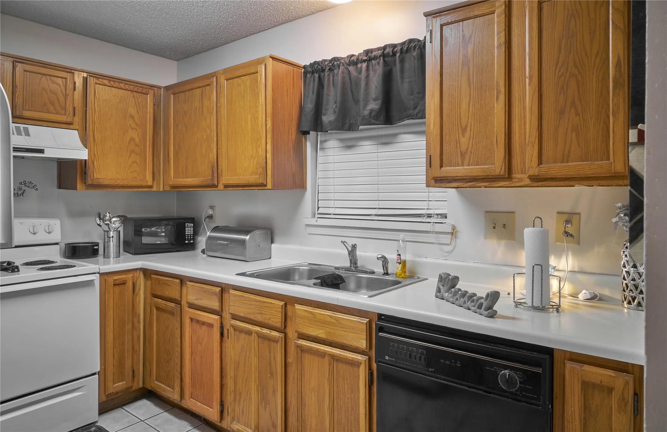 Kitchen with custom exhaust hood, black appliances, a textured ceiling, light tile floors, and sink