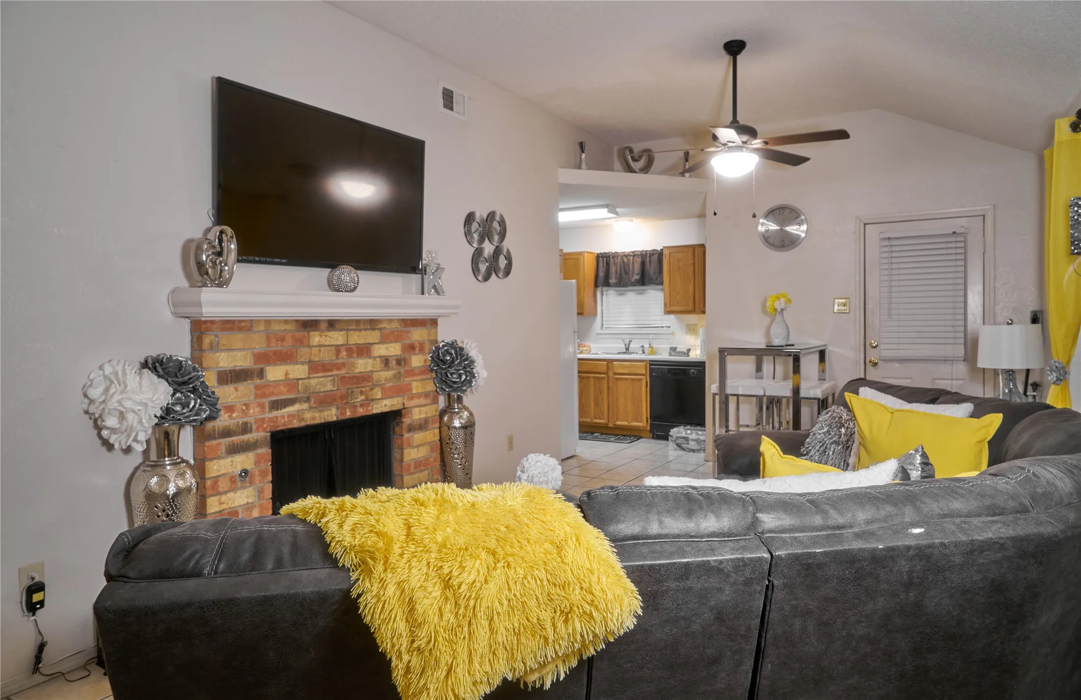Living room with lofted ceiling, a brick fireplace, light tile floors, and ceiling fan
