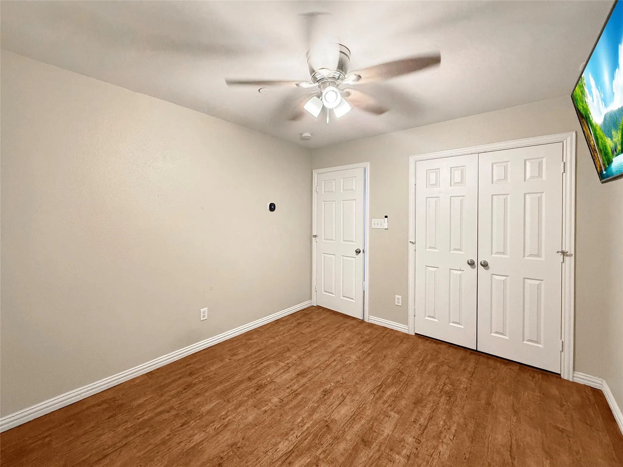 Wood-finish flooring, ceiling fan with integrated lighting, paneled doors, and white trim