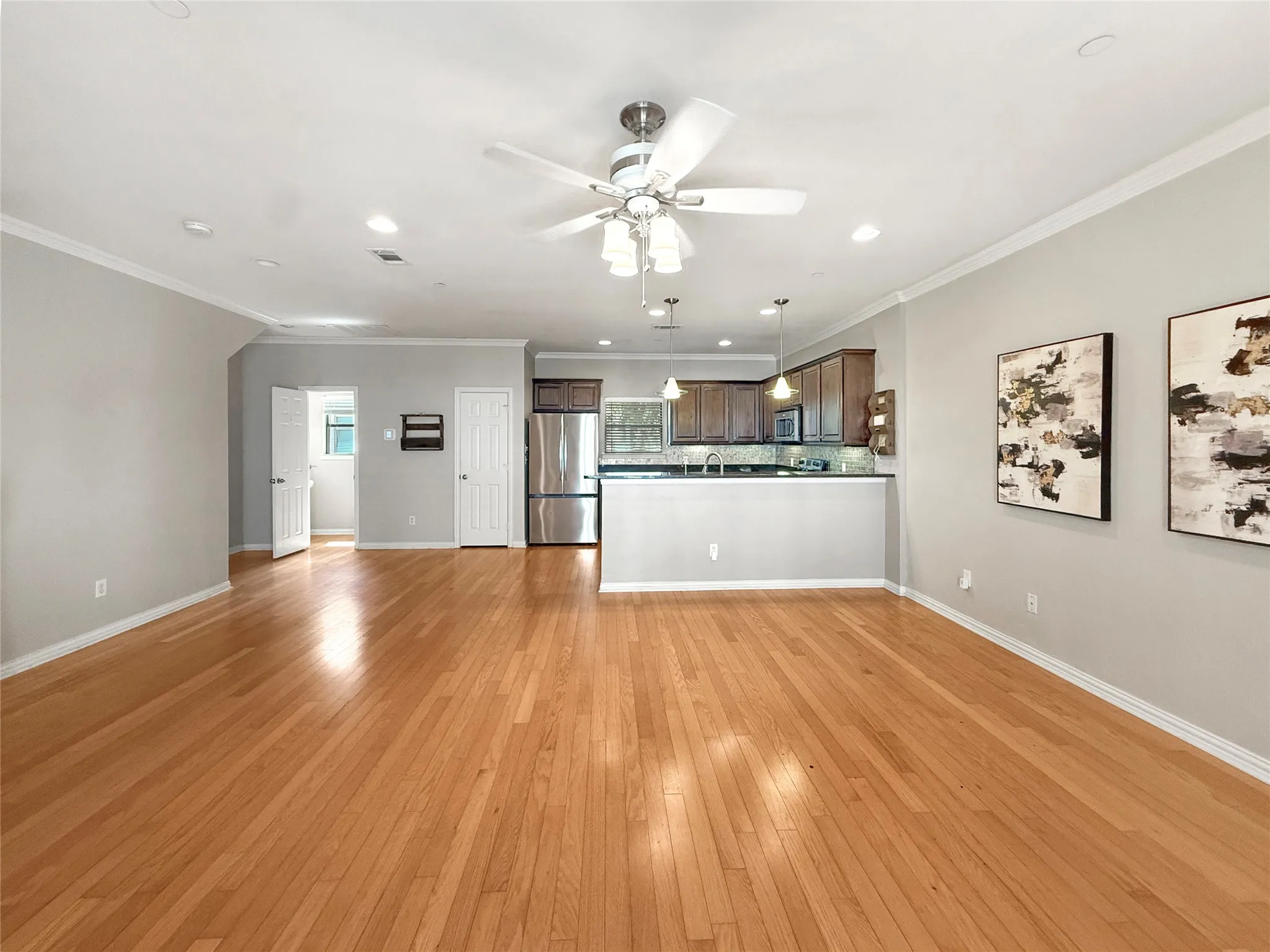 Open-concept living space featuring wood-finish flooring, a ceiling fan with integrated lighting, recessed lighting, and crown molding