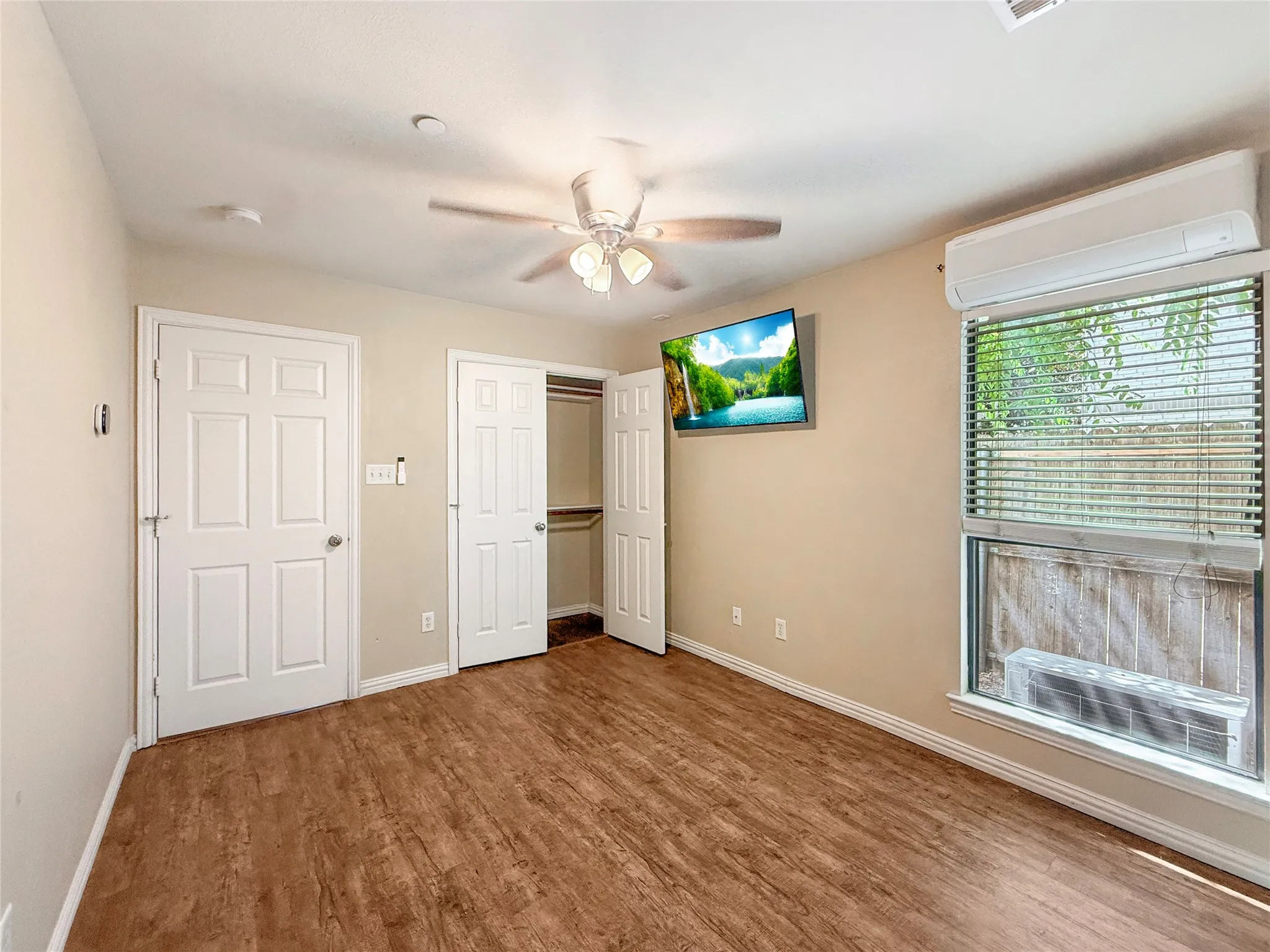 Wood-finish flooring, ceiling fan with integrated lighting, split air conditioning unit, and built-in closet with bi-fold doors
