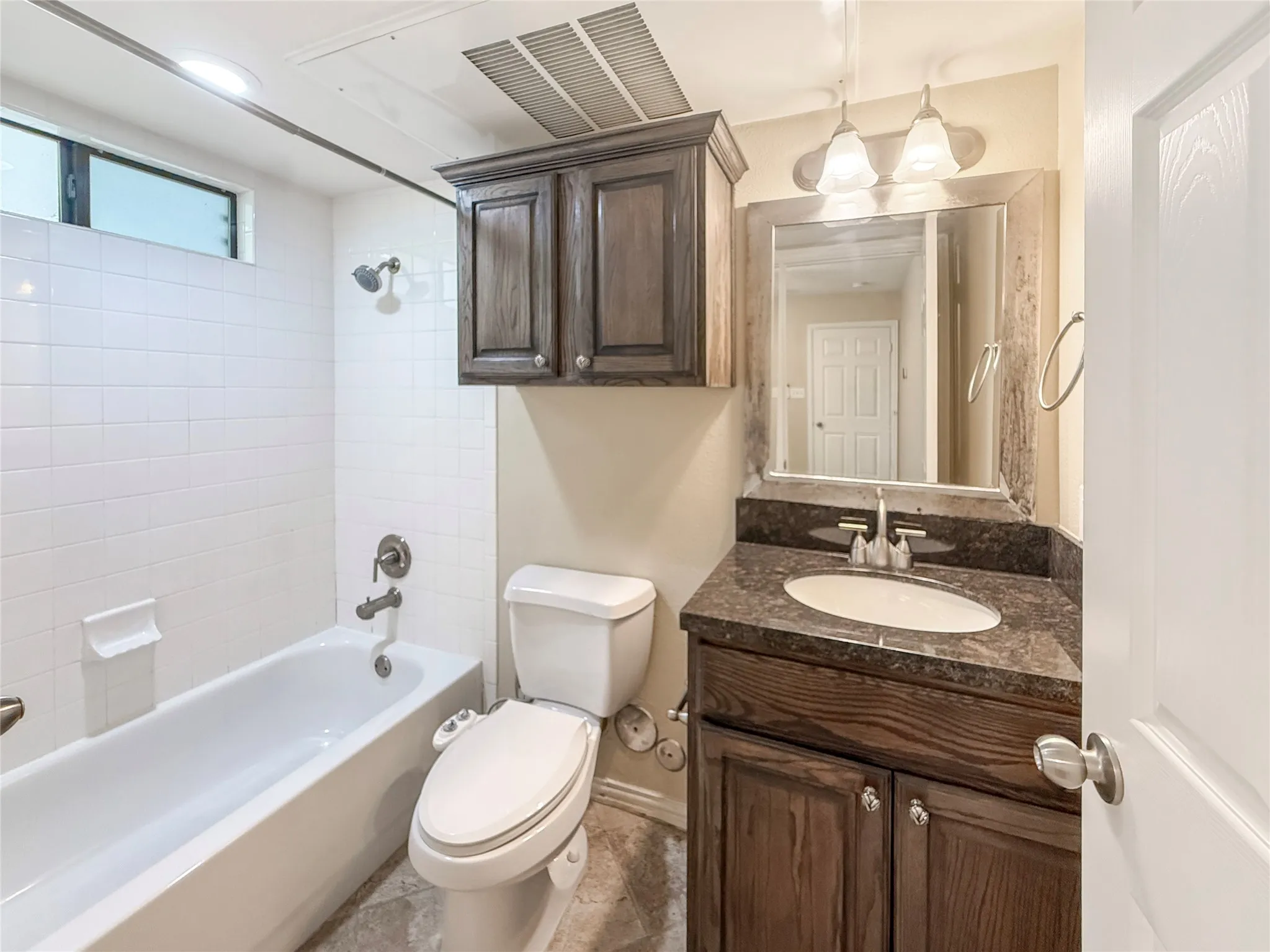 Bathroom featuring a white bathtub with tile surround, a dark wood-finish vanity with a countertop sink, and a framed mirror with overhead lighting