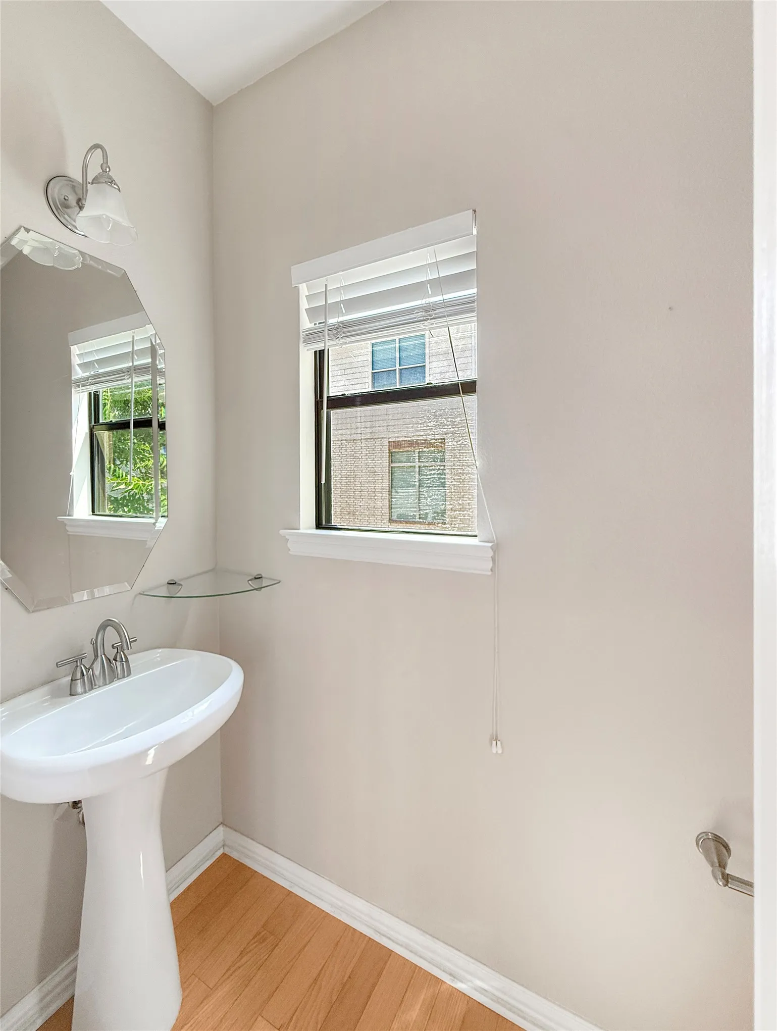 Pedestal sink with chrome faucet, octagonal wall mirror, and wood-finish flooring