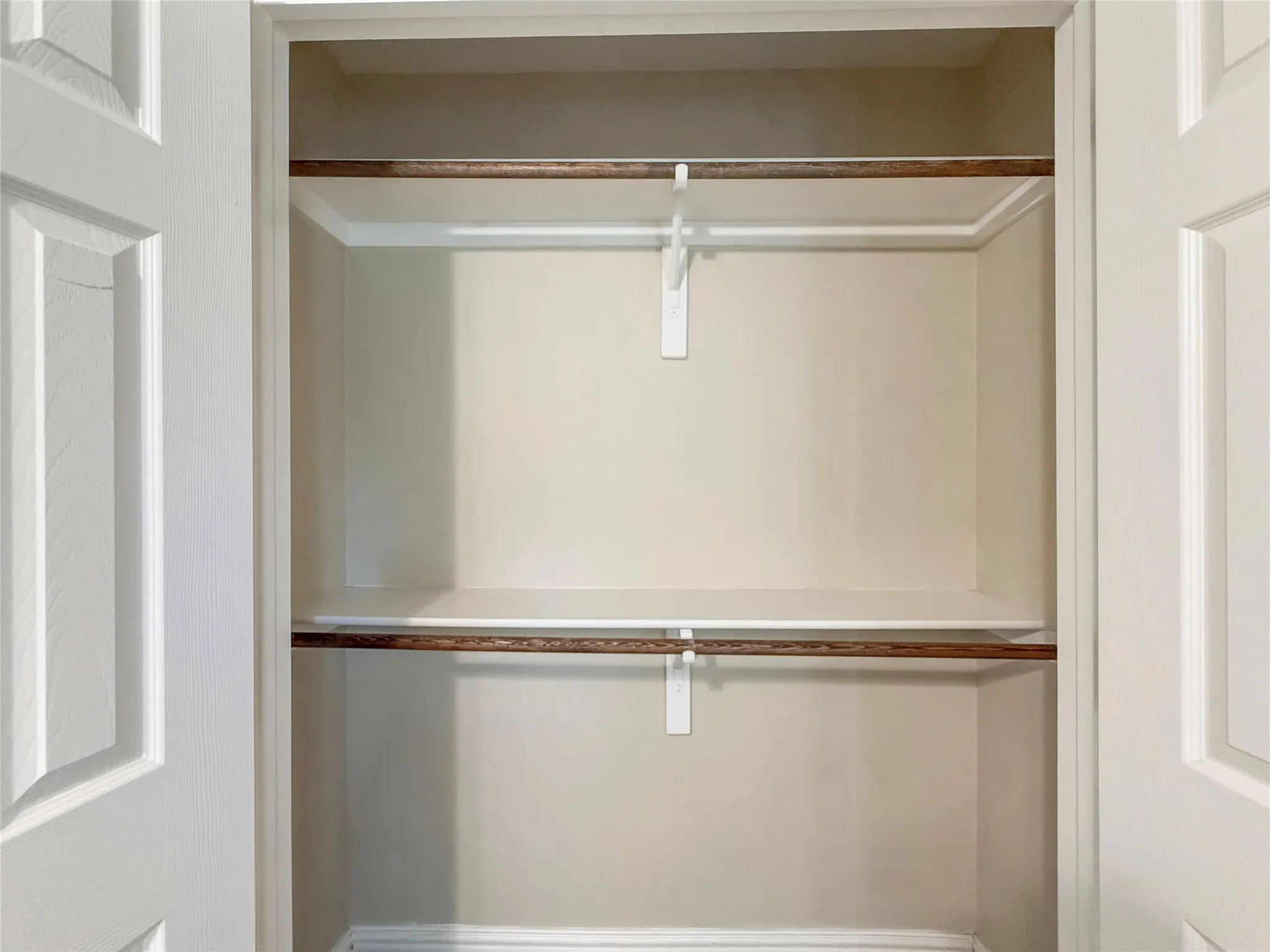 Recessed closet with two white shelves and two wood-finish hanging rods