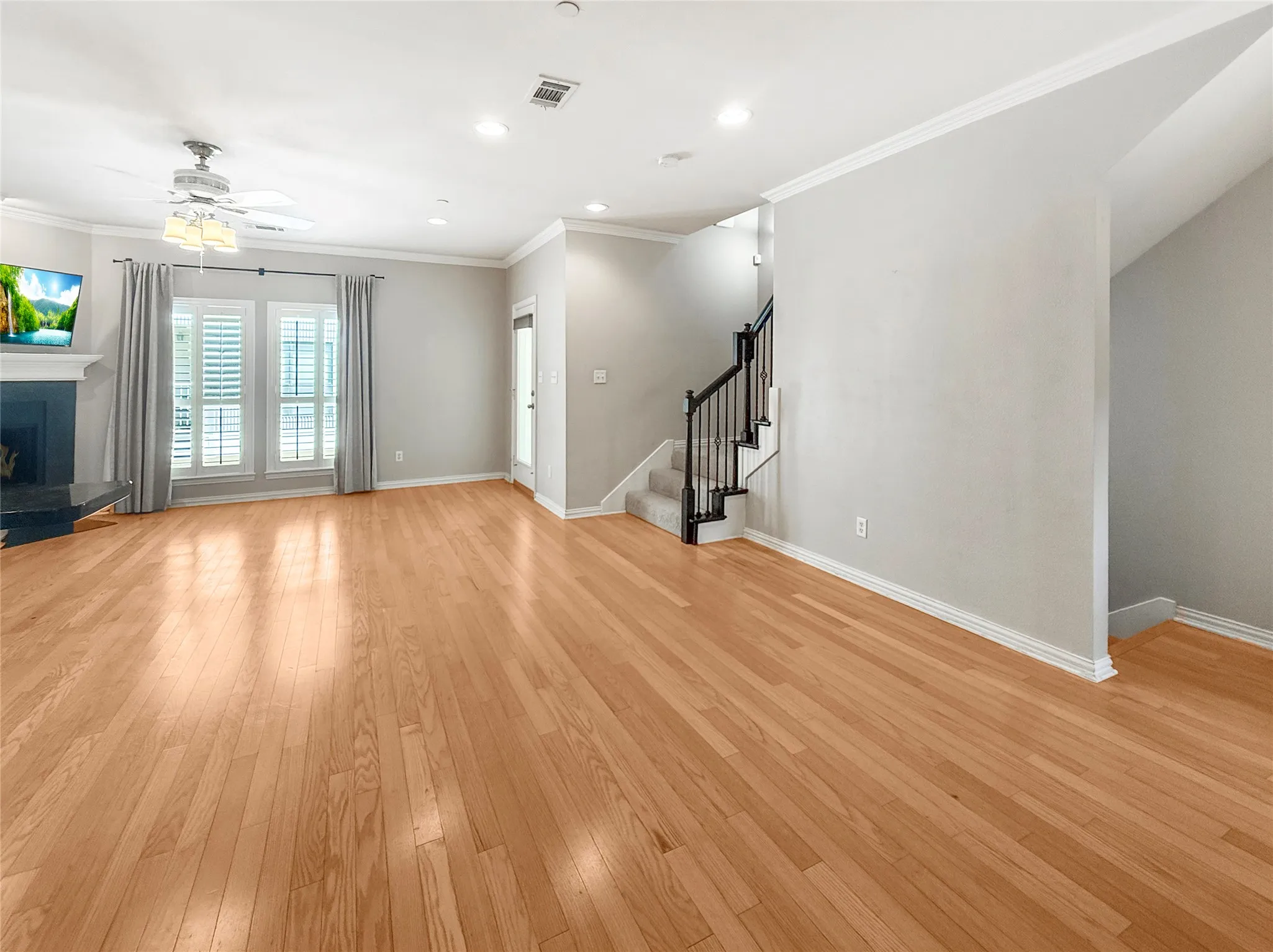 Hardwood-finish flooring throughout, a fireplace with a dark mantel, window shutters, recessed lighting, and a staircase with dark balusters