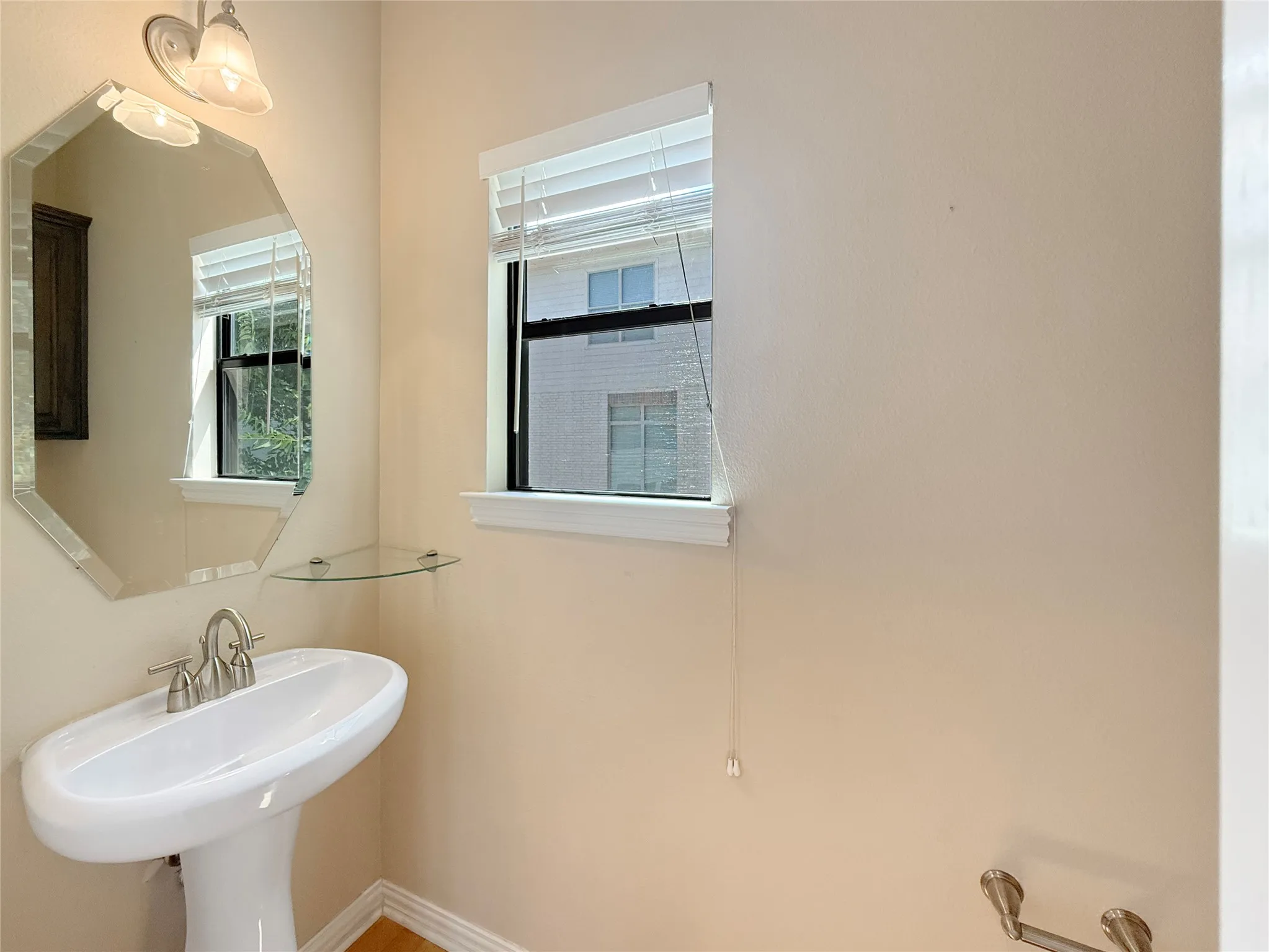 Pedestal sink with a brushed nickel faucet, an octagonal mirror, and wall-mounted lighting