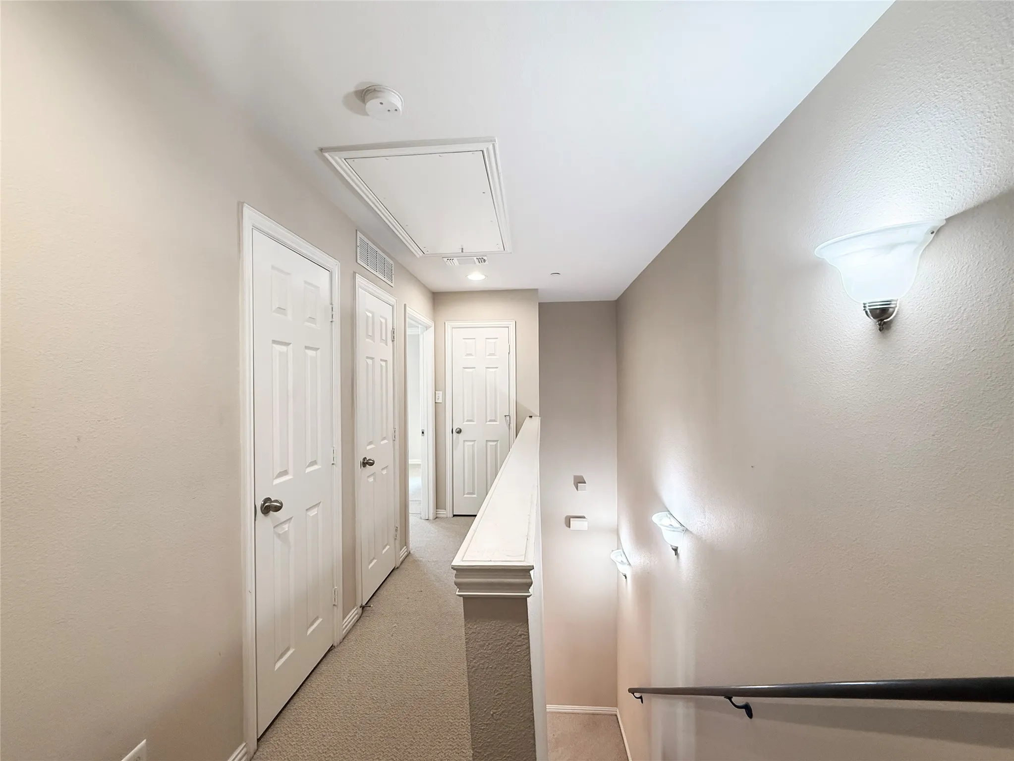 Carpeted hallway featuring multiple white paneled doors, recessed ceiling lighting, and wall-mounted sconces