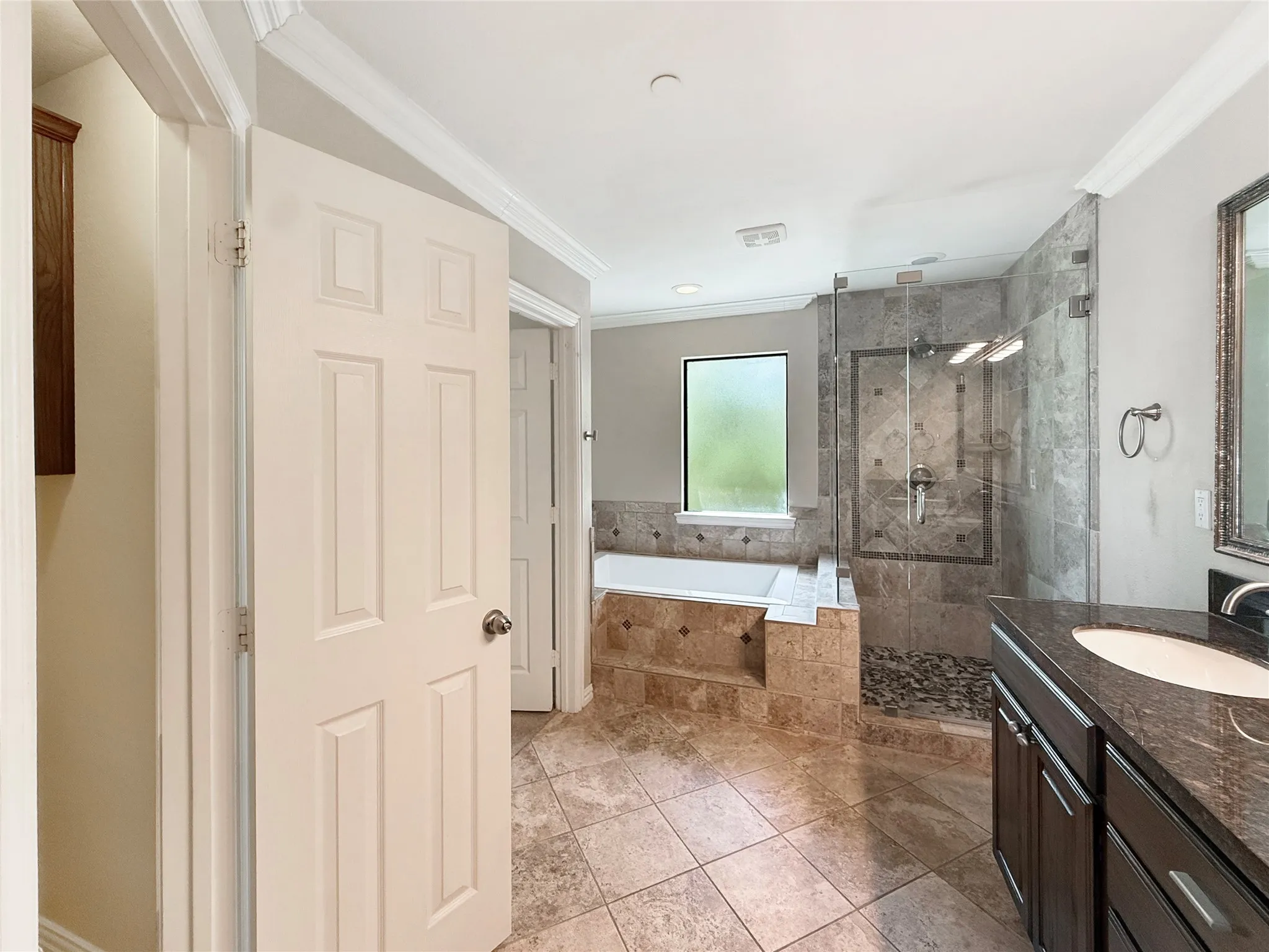 Glass-enclosed shower with pebble floor, soaking tub, dark wood vanity with granite countertop, and tile flooring