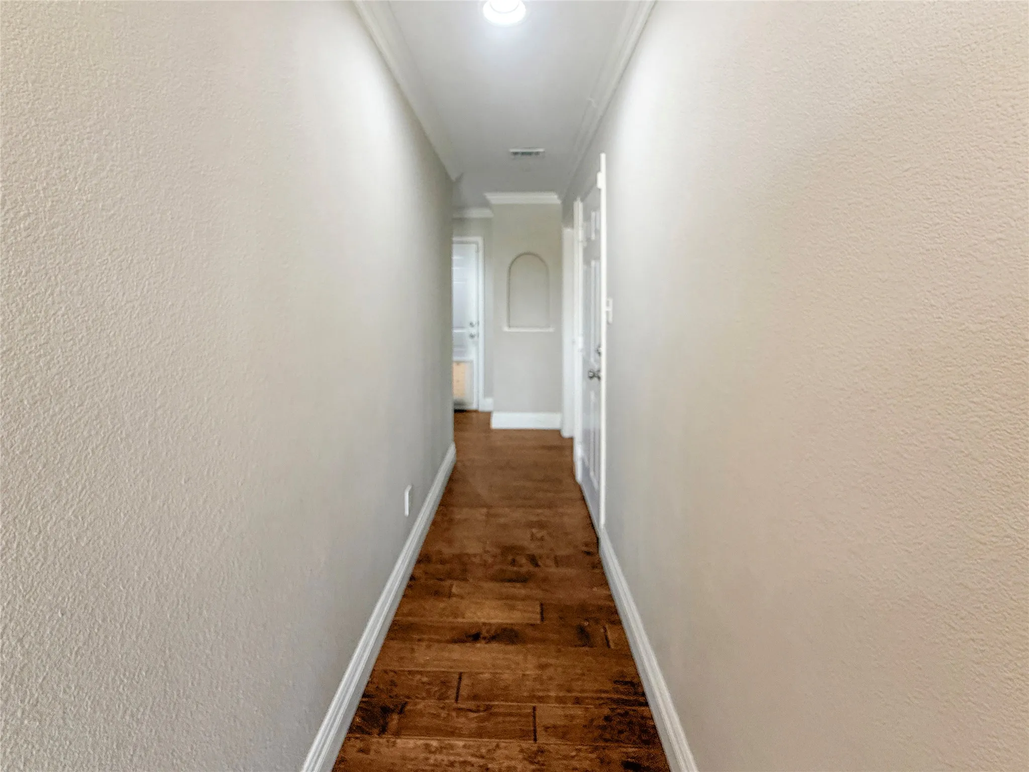 Hallway featuring wood-finish flooring, light-toned textured walls, crown molding, and a recessed arch niche