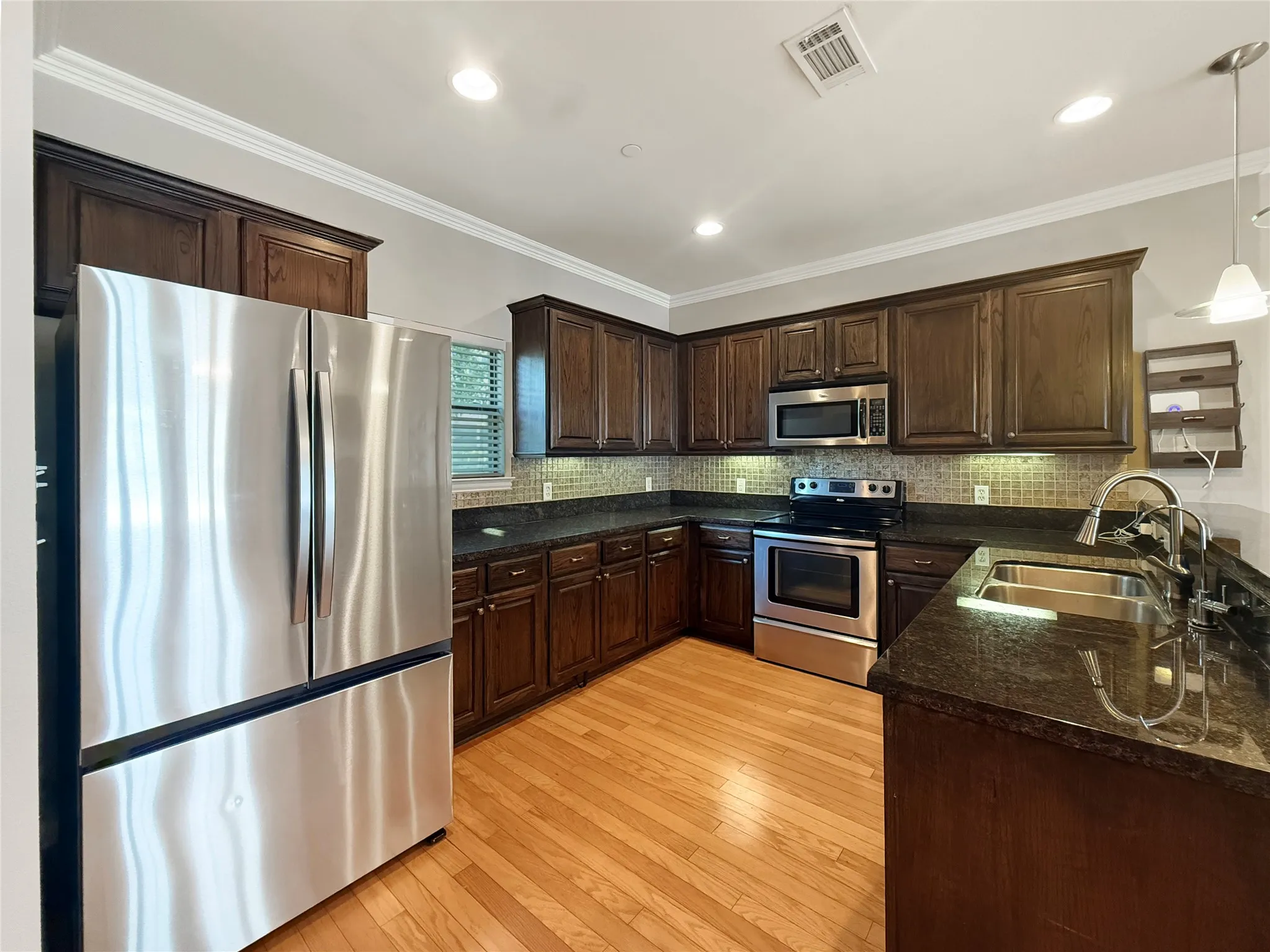 Kitchen featuring wood-finish flooring, dark wood cabinetry, stainless steel appliances, and dark countertops