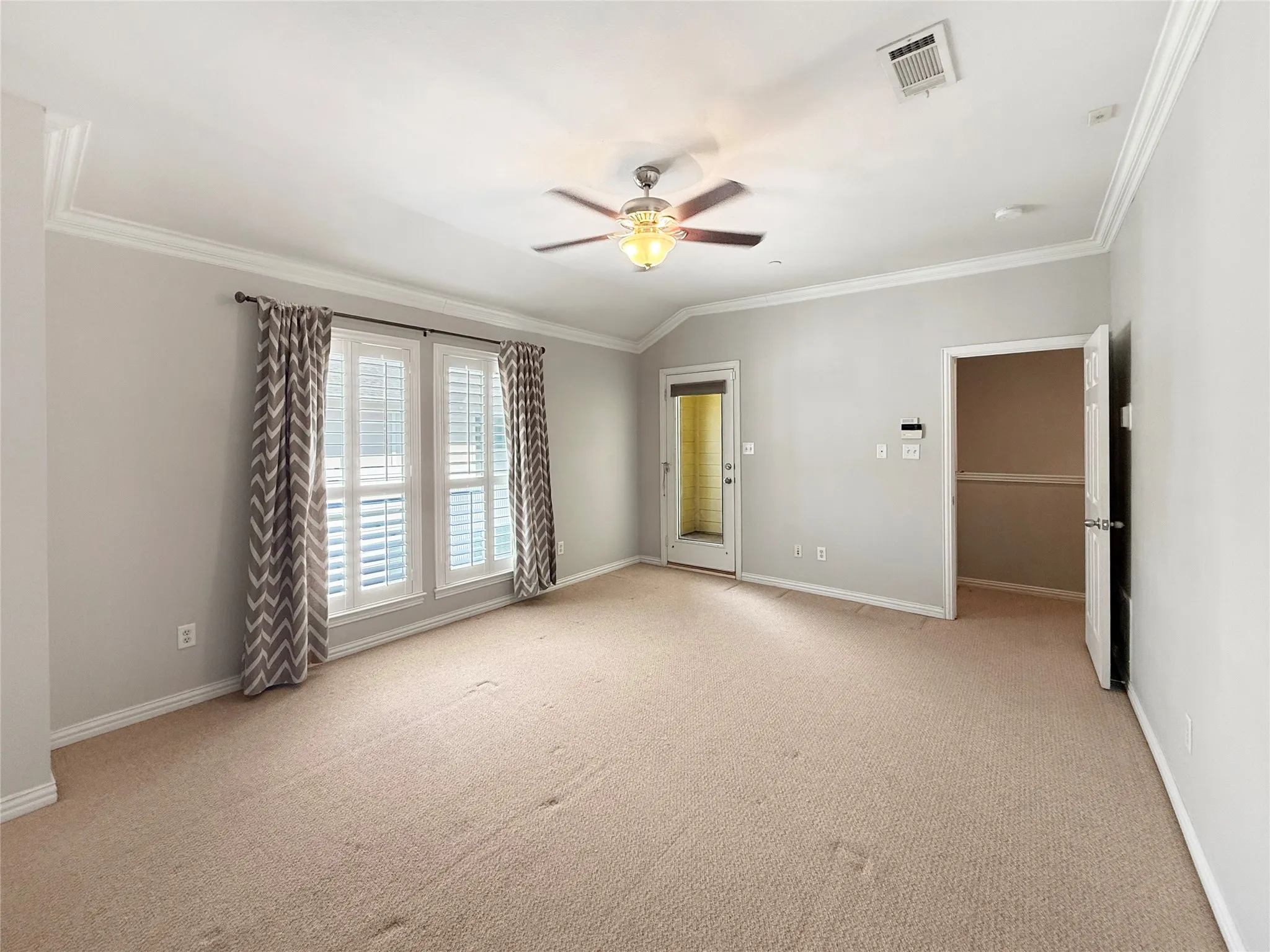 Carpeted room featuring a ceiling fan, crown molding, and a door leading to the exterior