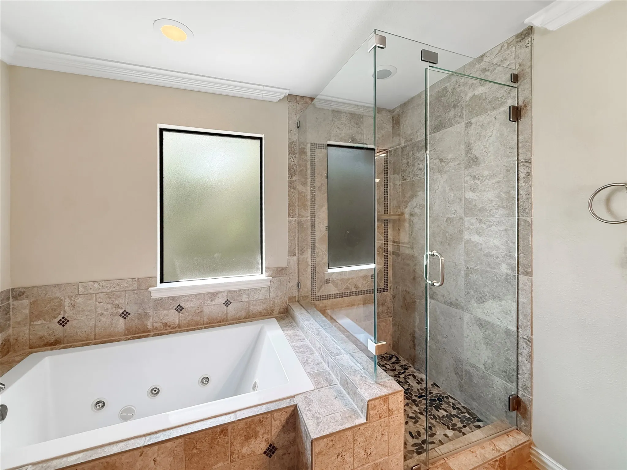 Jetted soaking tub, tiled surround with accent detailing, frameless glass shower enclosure, pebble tile shower floor, and recessed lighting