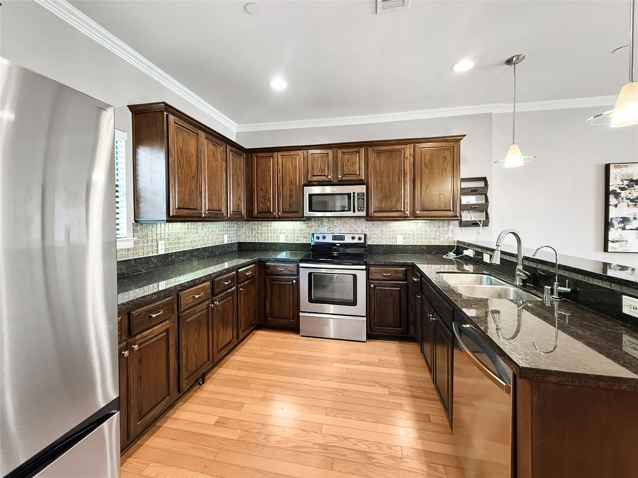 U-shaped kitchen featuring wood-finish cabinetry, dark countertops, a mosaic tile backsplash, stainless steel appliances, and wood-finish flooring