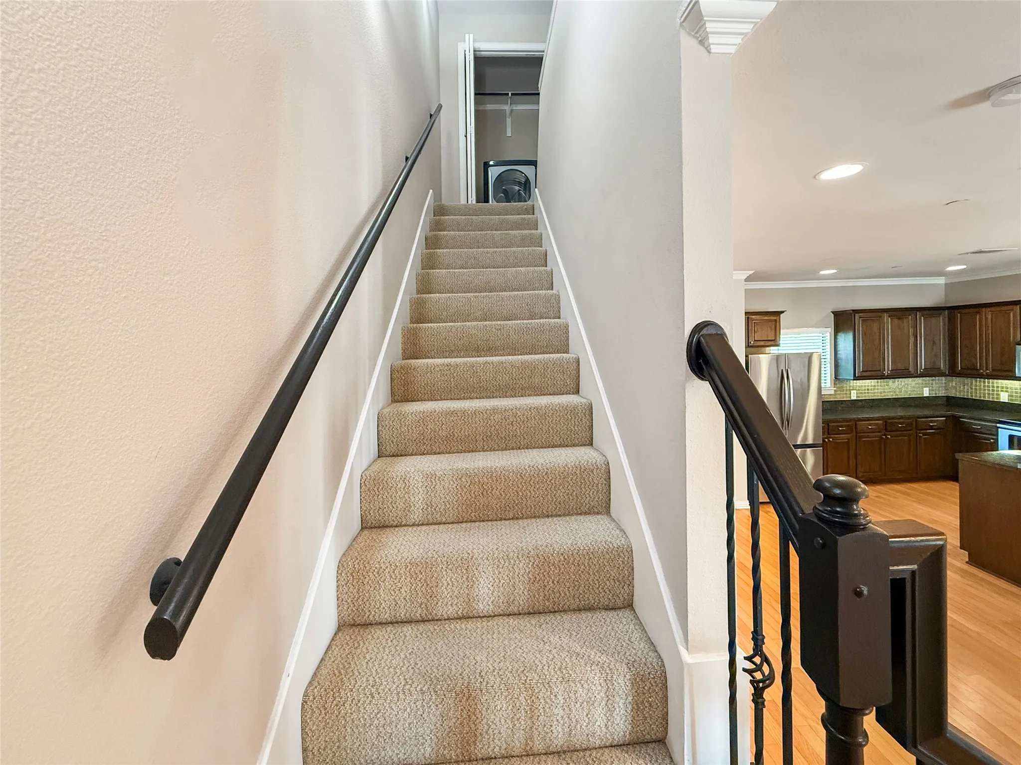 Carpeted staircase featuring a black metal handrail and decorative wrought iron balusters