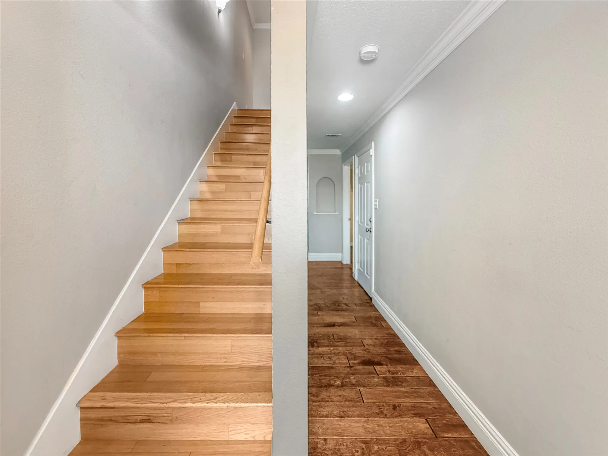 Hardwood stairs with a natural wood handrail, crown molding, recessed lighting, wood-finish flooring, and a decorative wall niche