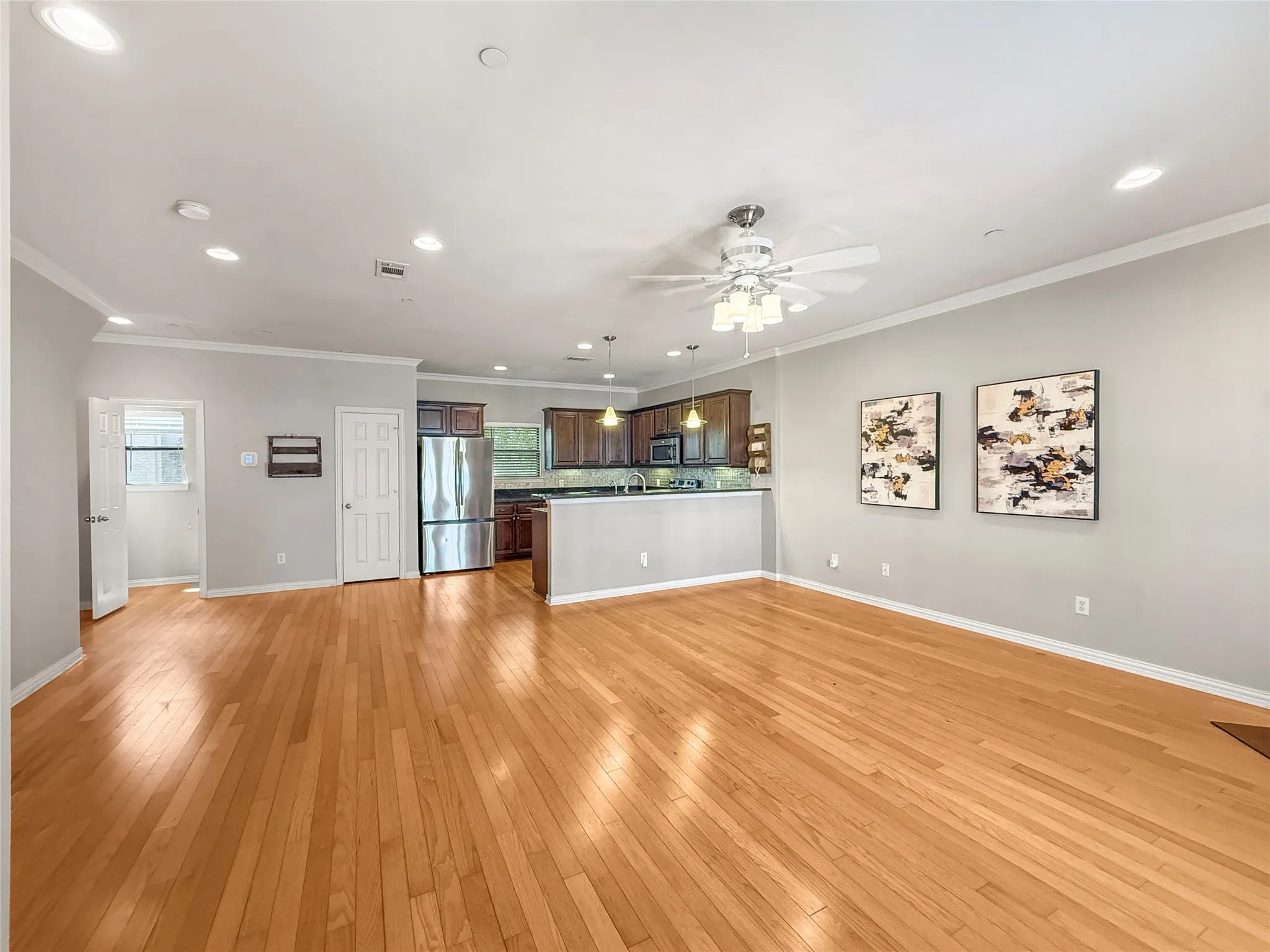 Open-concept living area with wood-finish flooring, recessed lighting, and crown molding