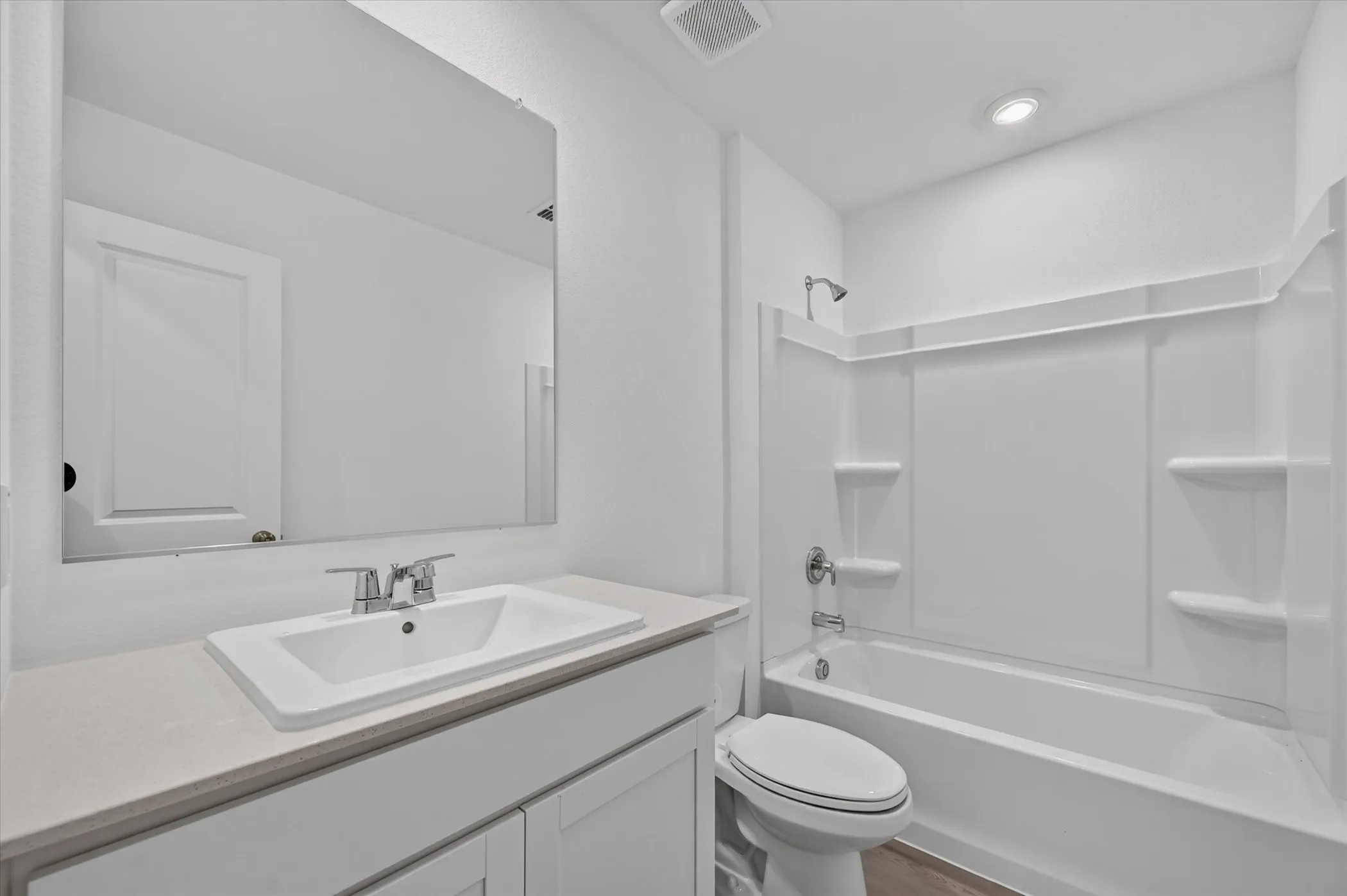 White bathroom vanity with an integrated sink and chrome faucet, large frameless mirror, and a full bathtub with a shower and integrated shelving
