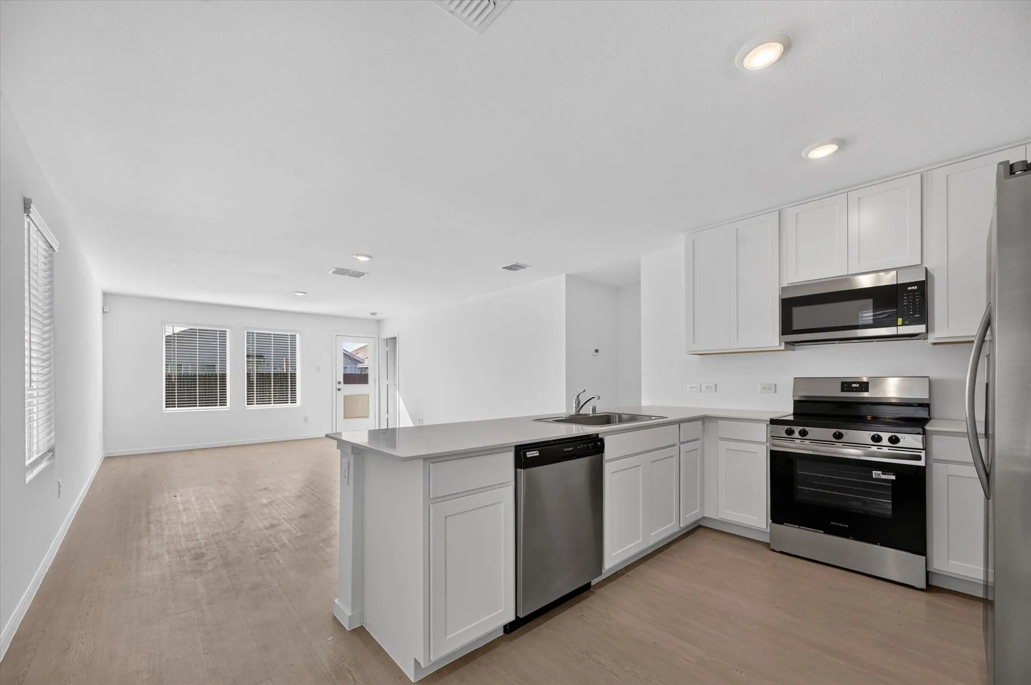 Open-concept kitchen with white shaker cabinetry, stainless steel appliances, light-toned countertops, and wood-finish flooring
