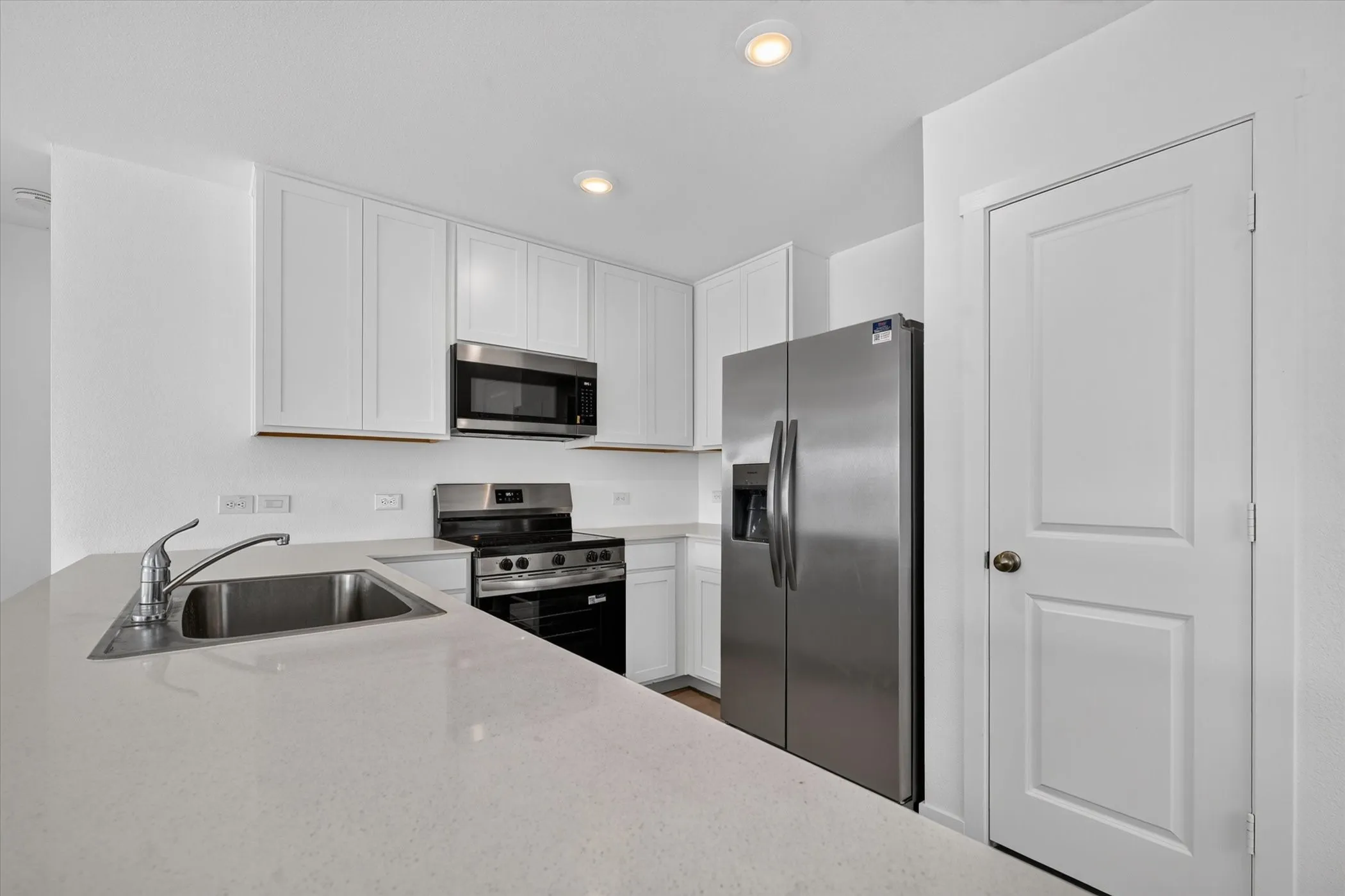 White shaker-style cabinetry, stainless steel appliances, dual basin sink with a single-handle faucet, and light-toned countertops