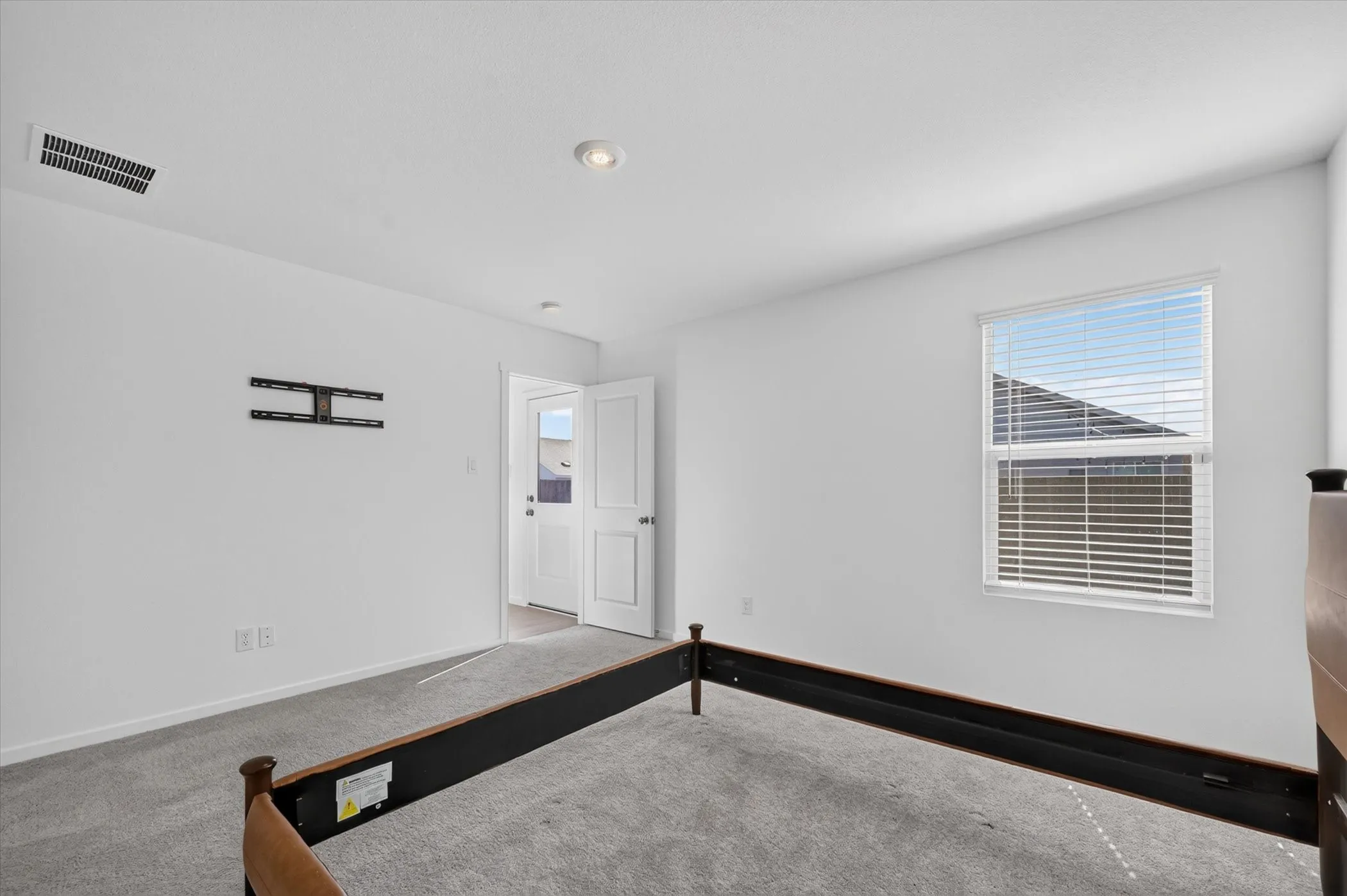 Recessed lighting with a ceiling vent, wall-mounted television bracket, neutral carpeting, and a window with blinds