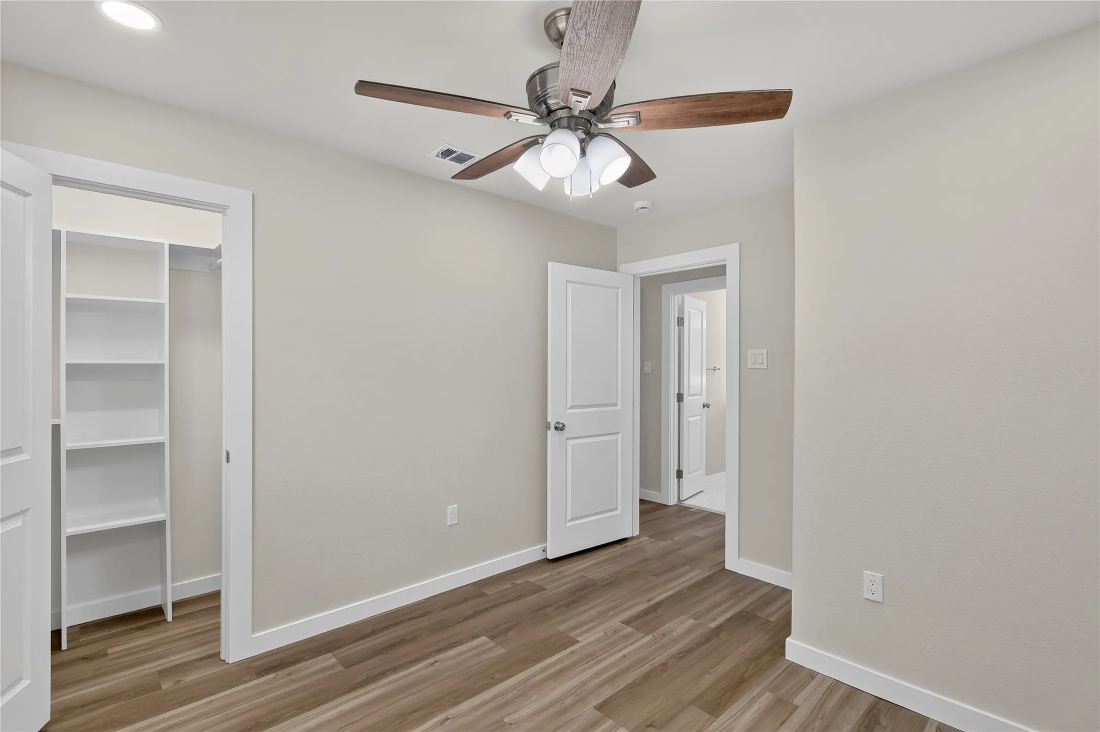 Wood-finish flooring, recessed ceiling lighting, ceiling fan with integrated light fixture, white trim, and a built-in closet organization system