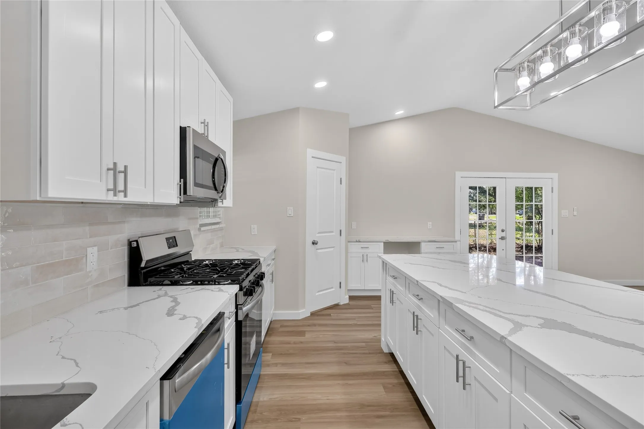 Kitchen featuring white cabinetry, light-toned backsplash, stainless steel appliances, and a large island with a light-colored countertop