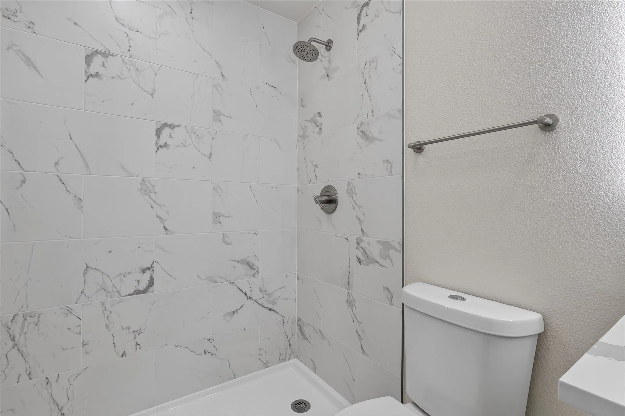Shower with marble-look tile surround, brushed nickel fixtures, and a glass partition