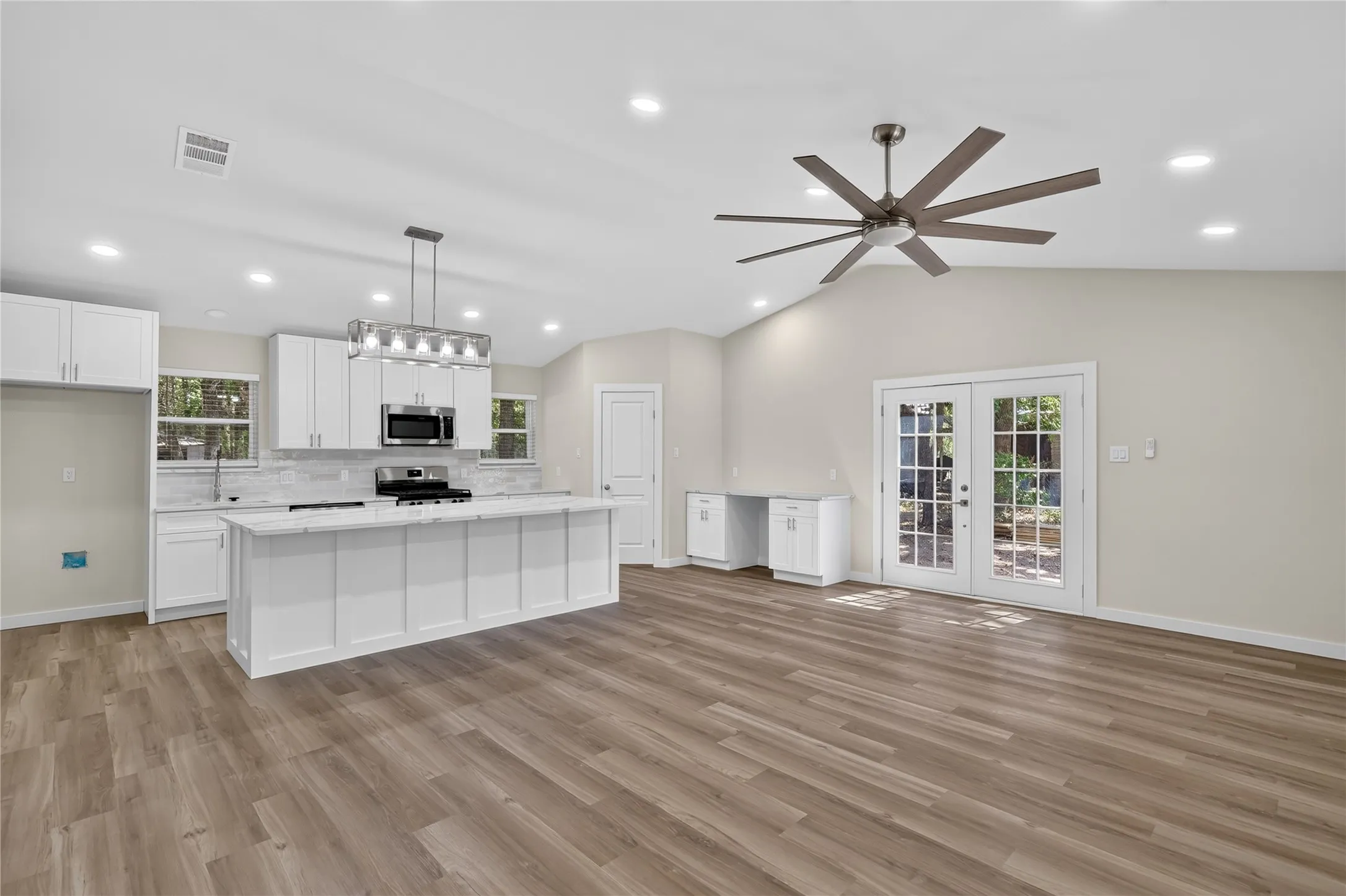 Modern kitchen featuring white cabinetry, a large center island with a quartz countertop, stainless steel appliances, and a tile backsplash