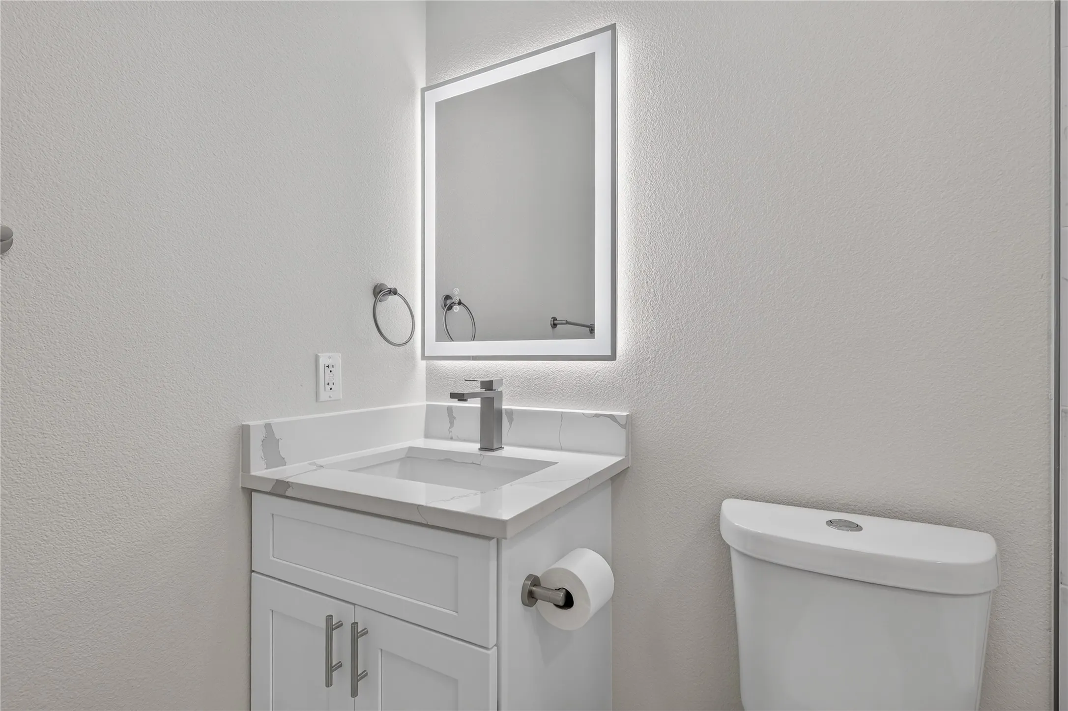 White vanity with shaker-style cabinetry, a built-in sink, and a countertop featuring veining