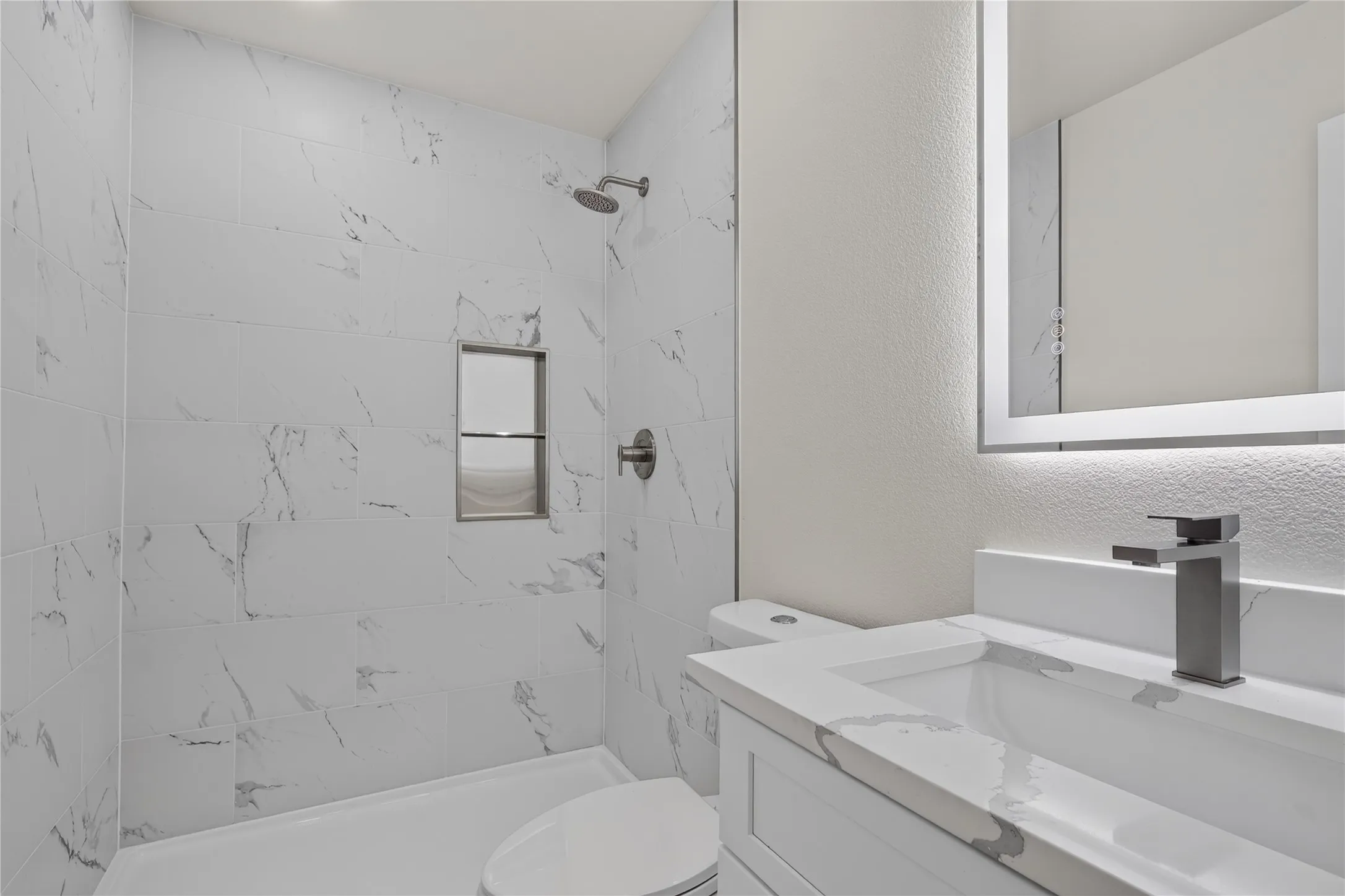 White vanity with integrated sink, matte gray faucet, and illuminated mirror