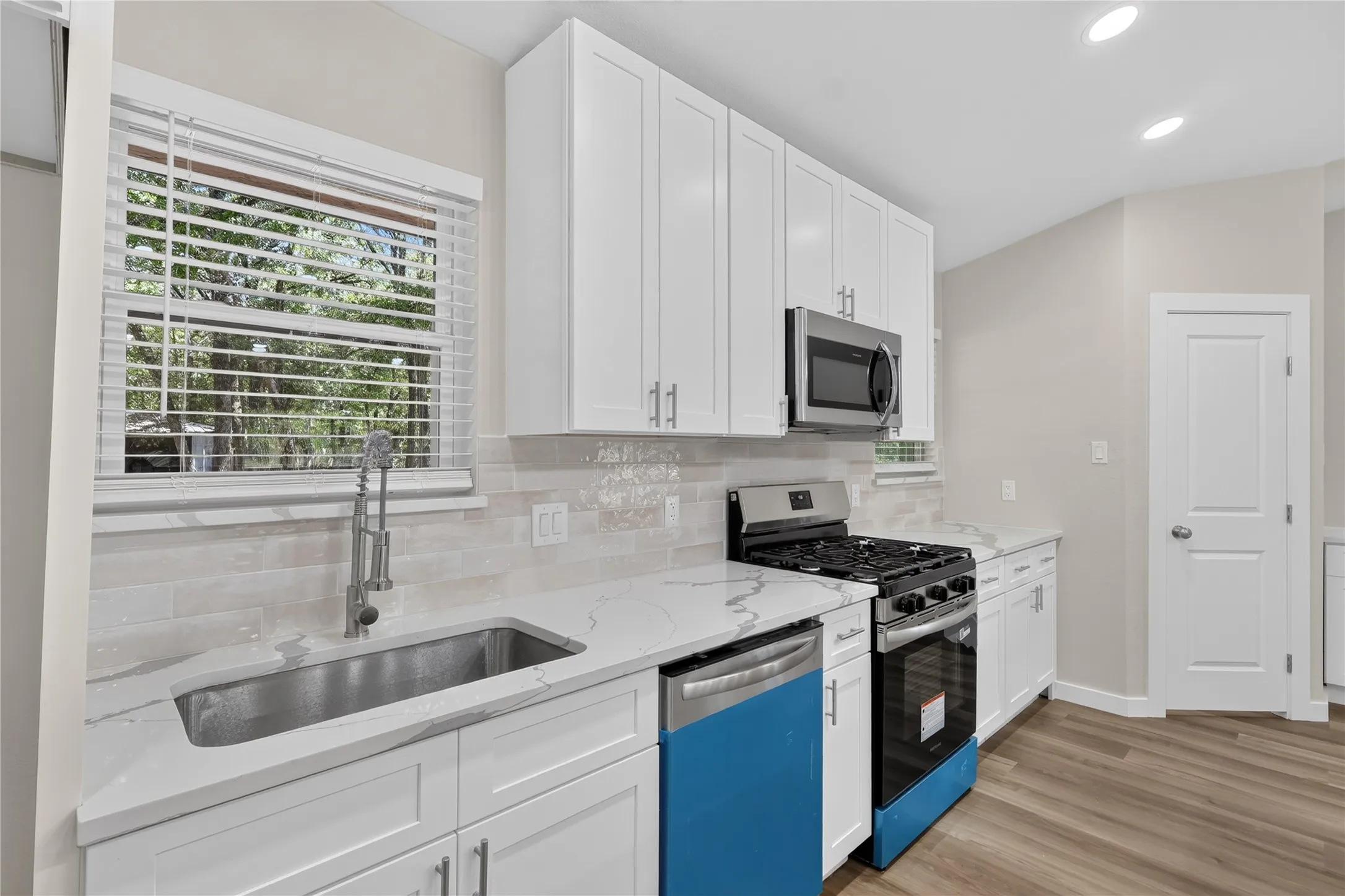 White shaker cabinetry, stainless steel appliances, undermount sink, quartz countertops, and wood-finish flooring