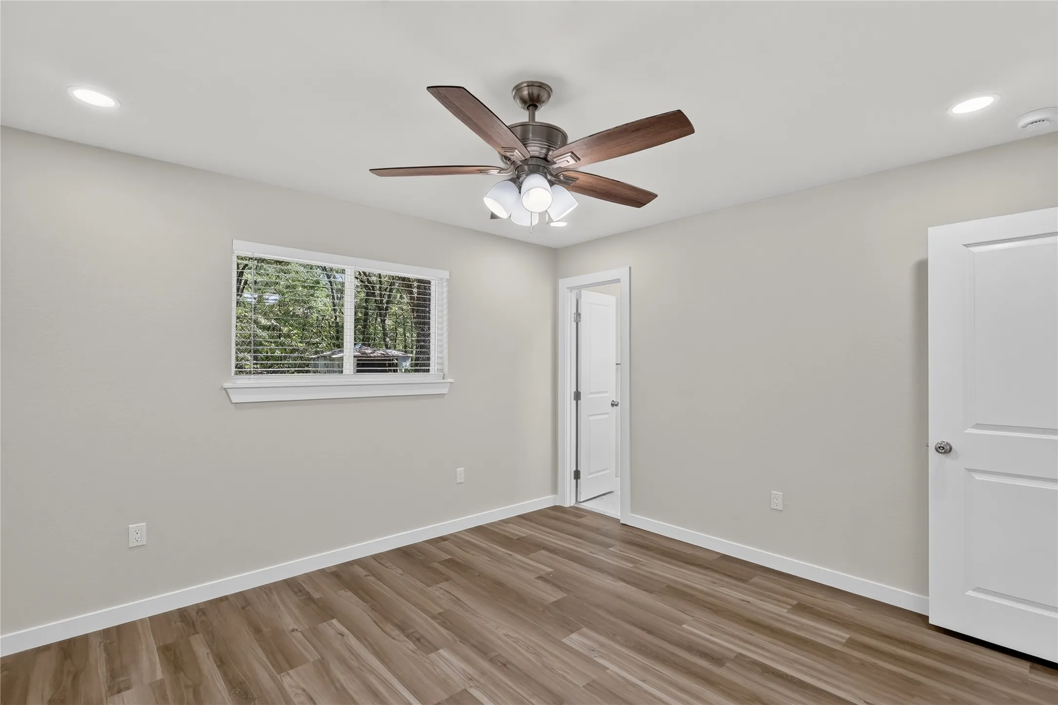 Wood-finish flooring, recessed lighting, ceiling fan with integrated light fixture, window with blinds, and a paneled interior door
