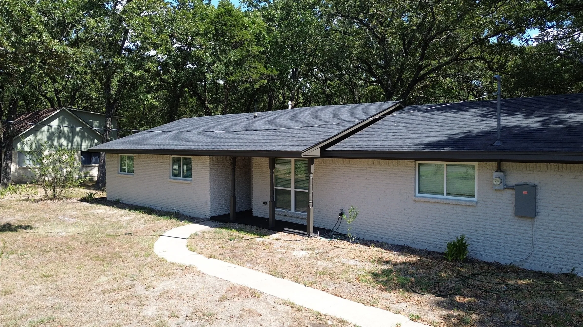 Exterior featuring light-colored brick, dark shingle roof, and a concrete pathway