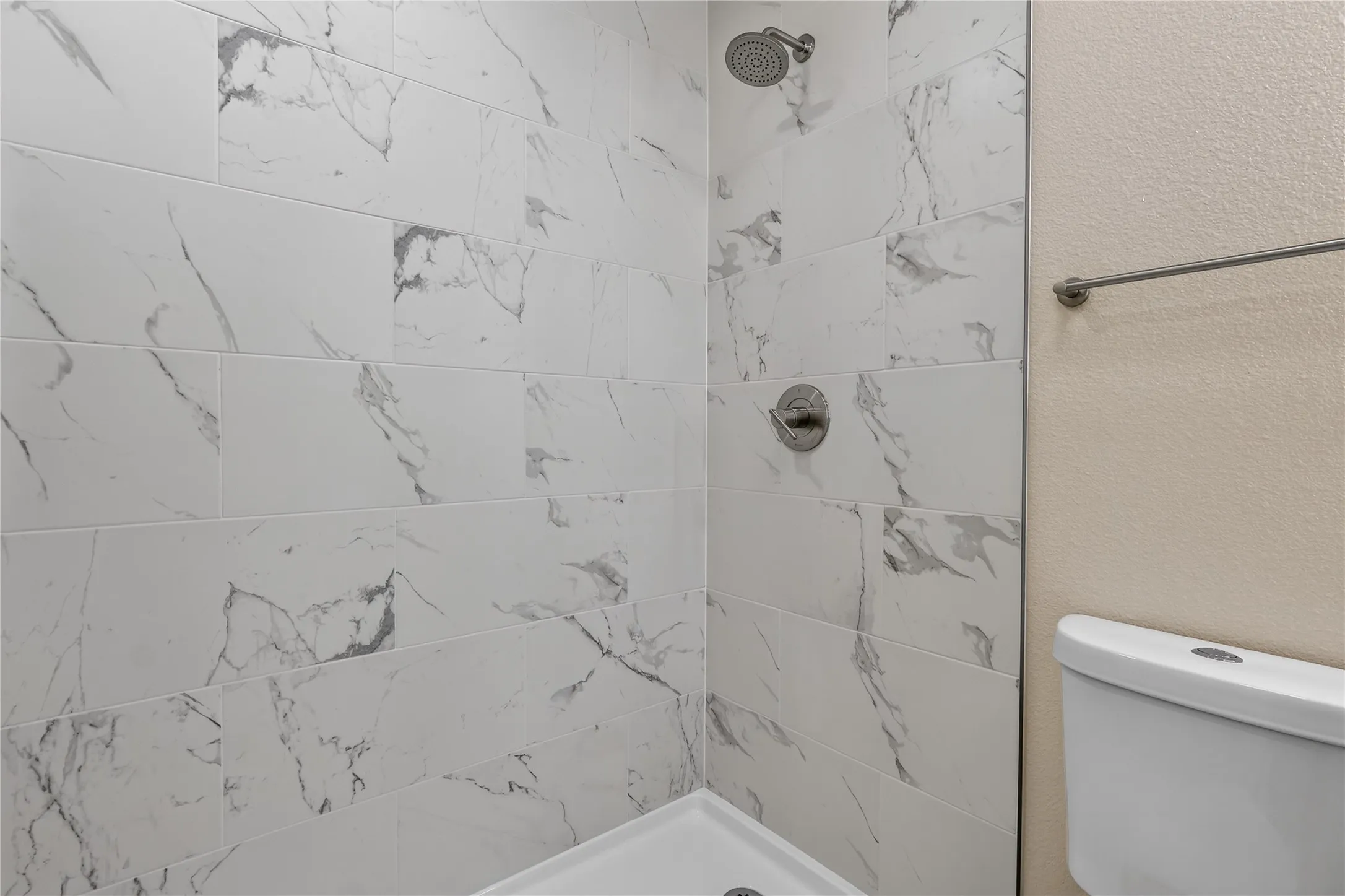 Shower with large format tile walls, brushed nickel fixtures, and a white shower pan