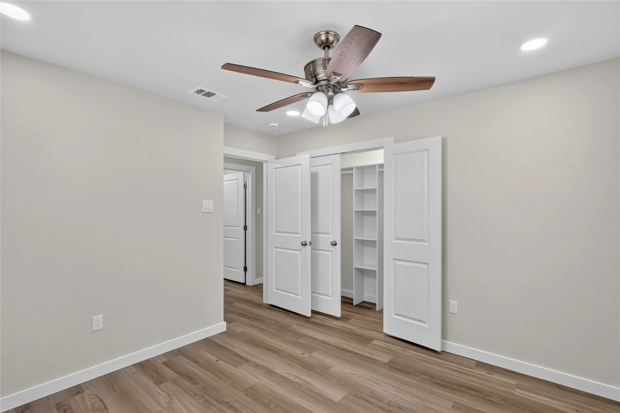 Wood-finish flooring, recessed lighting, ceiling fan with light fixture, white bi-fold closet doors, and built-in closet shelving