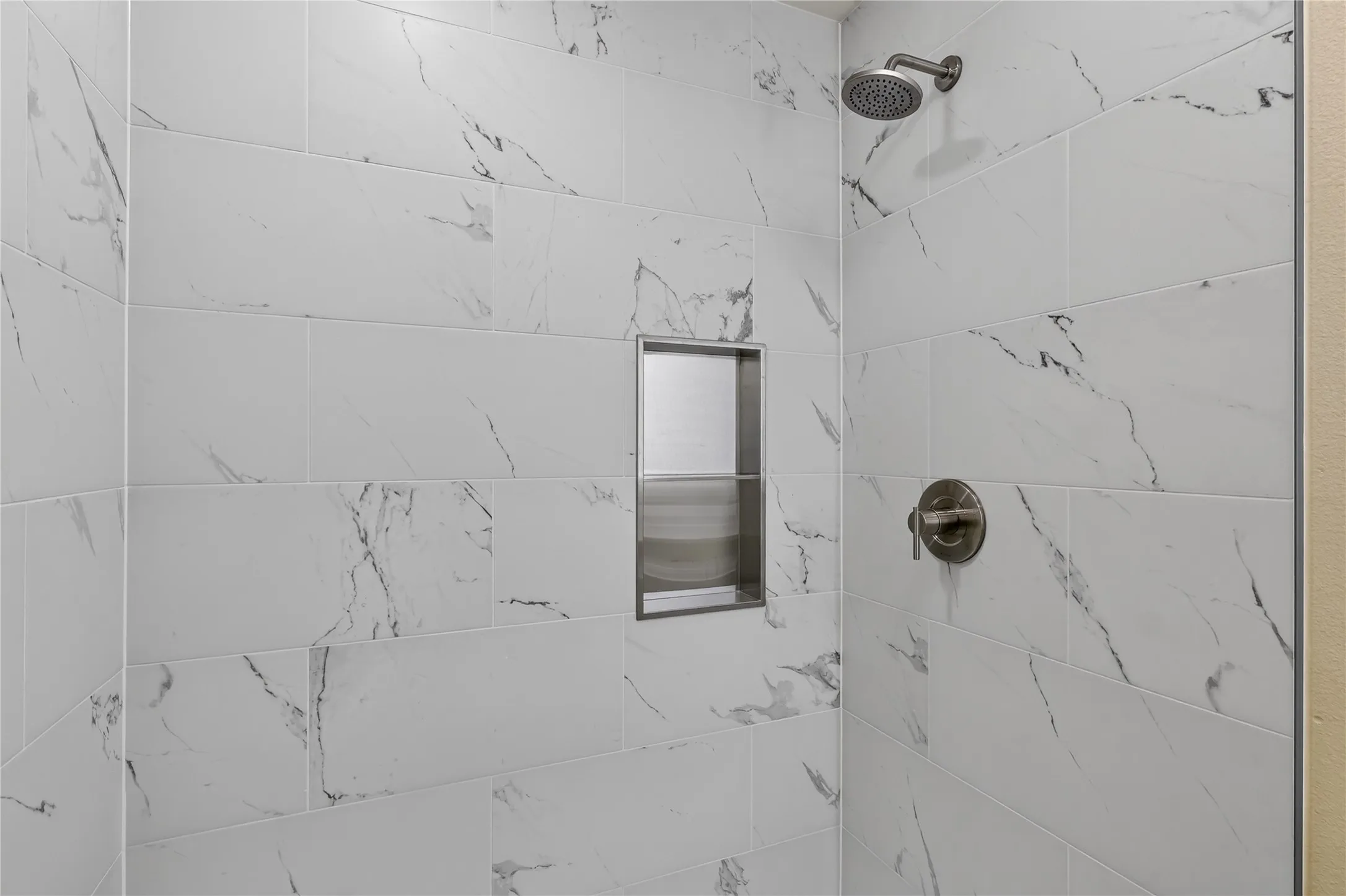 Shower featuring white subway tile with gray veining, built-in recessed niche, and a bronze shower head and control
