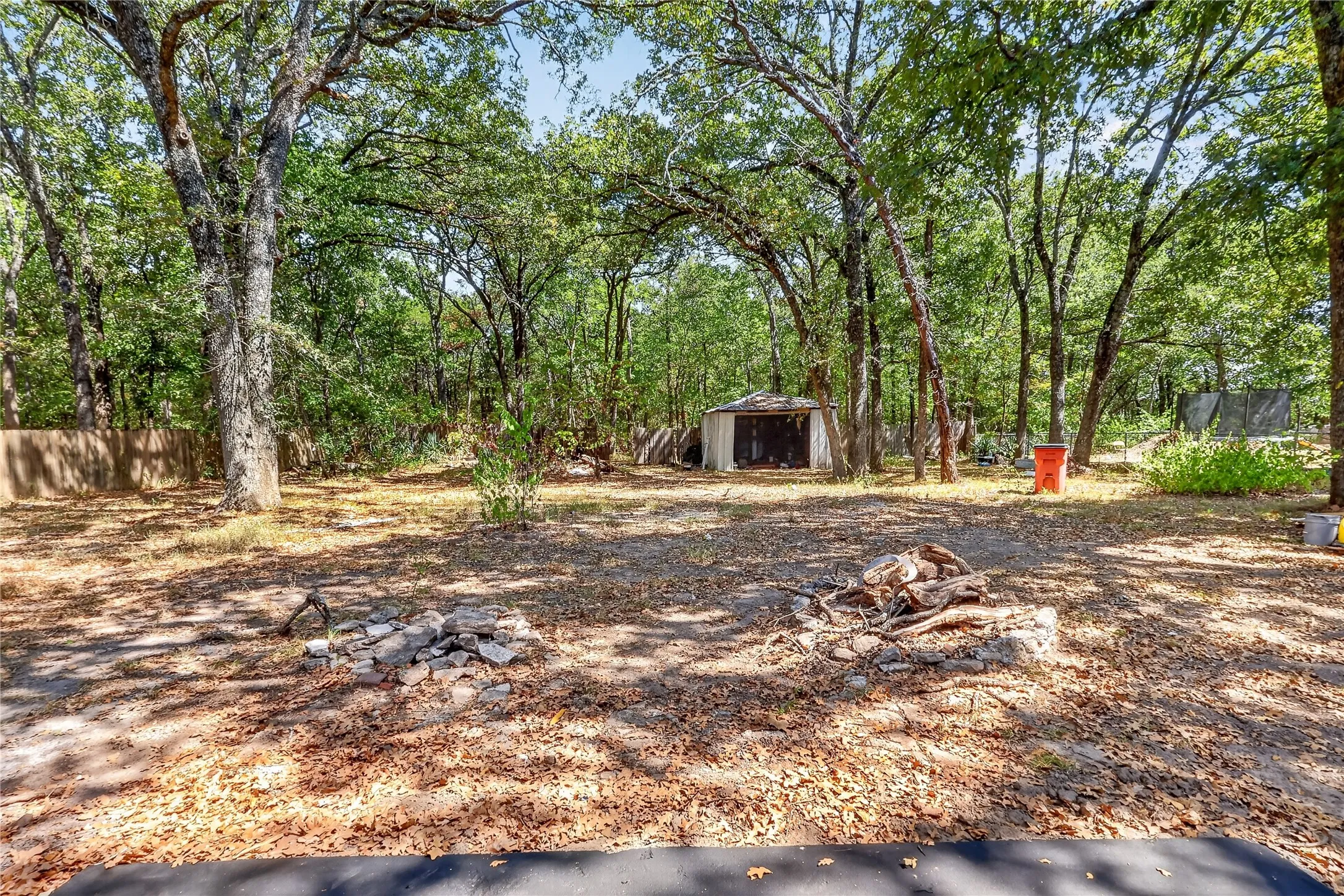 Wooded lot featuring mature trees, fire pit areas, and a detached storage shed