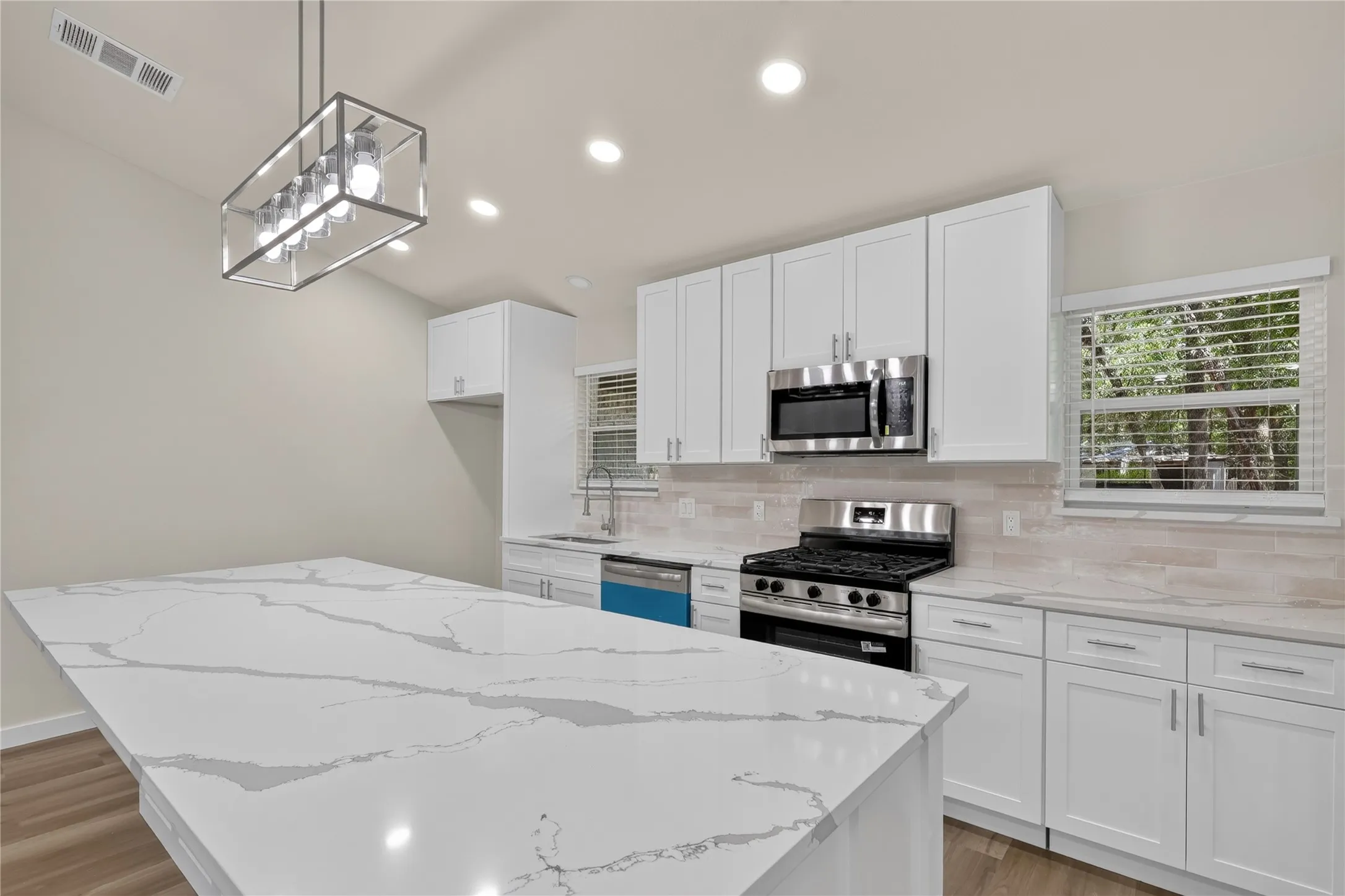 Kitchen featuring a spacious island with a light-toned countertop, white cabinetry, stainless steel appliances, and a tile backsplash