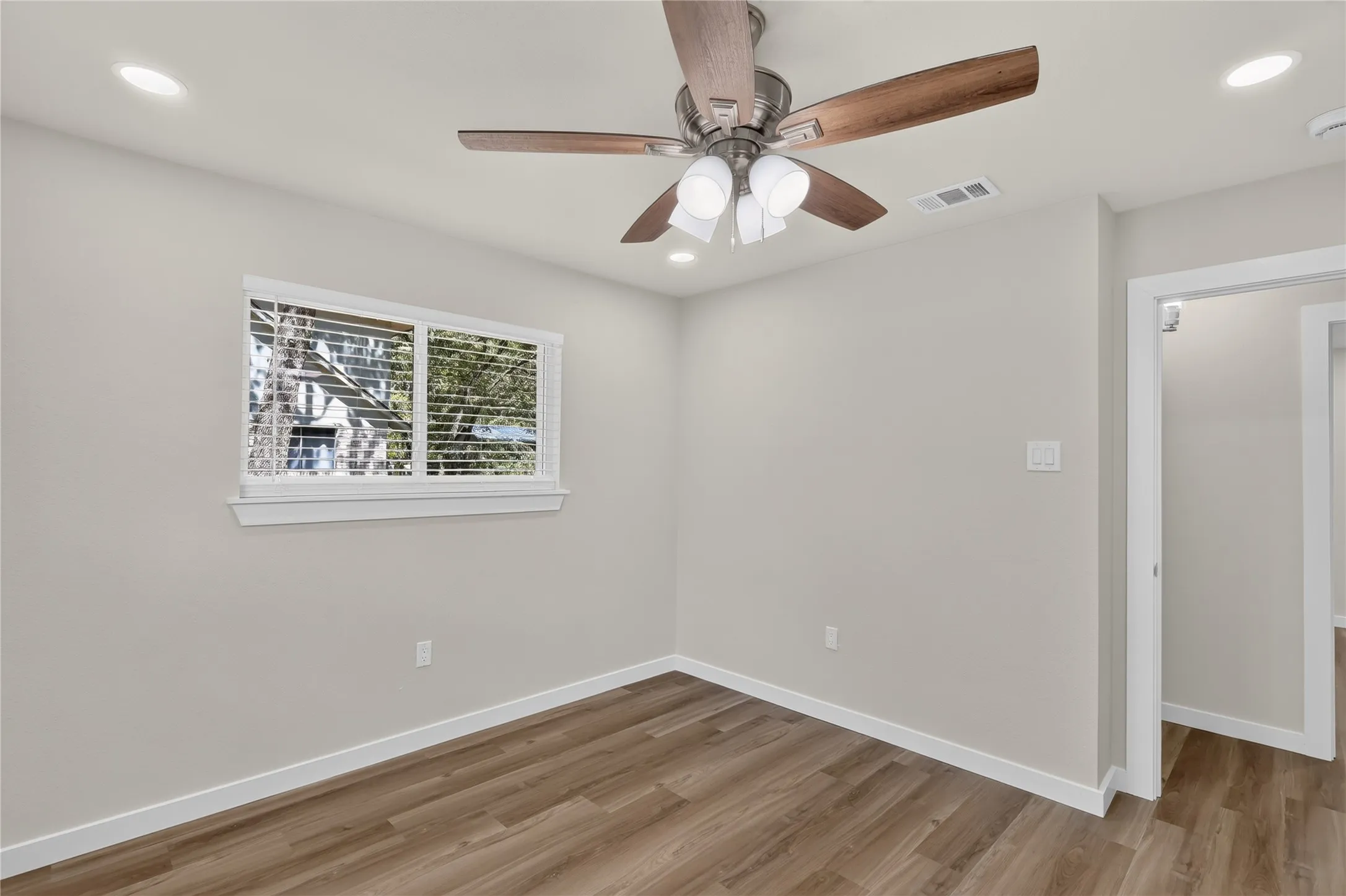 Wood-finish flooring with white trim, recessed lighting, and a ceiling fan with integrated lighting