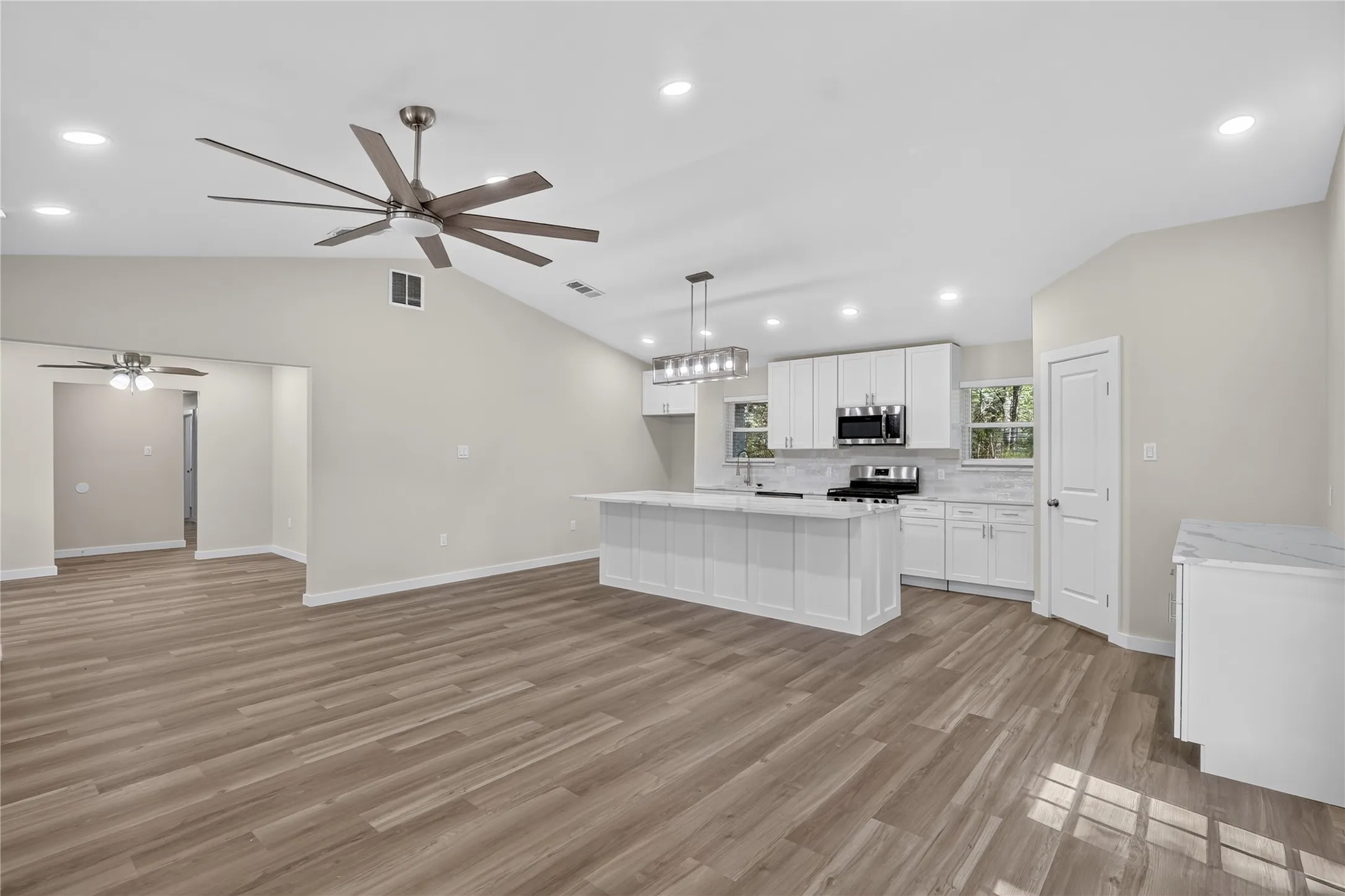 Vaulted ceiling, recessed lighting, wood-finish flooring, white shaker cabinetry, and stainless steel appliances