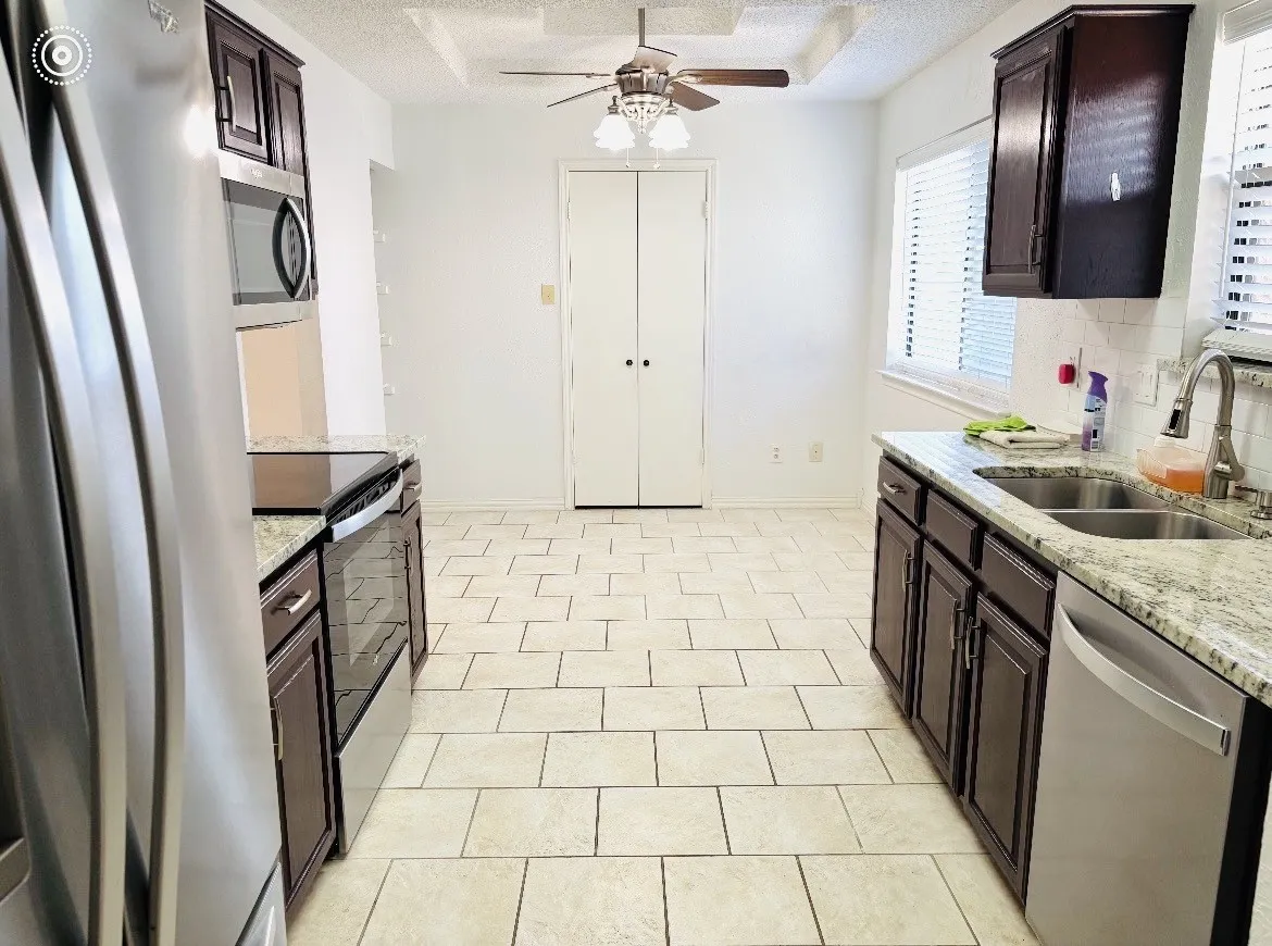 Kitchen featuring stainless steel appliances, dark wood-finish cabinetry, light-toned tile flooring, light-toned countertops, and a ceiling fan