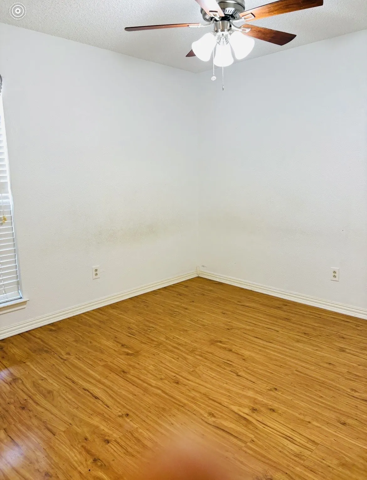 Wood-finish flooring with white baseboards, complemented by a ceiling fan with integrated lighting